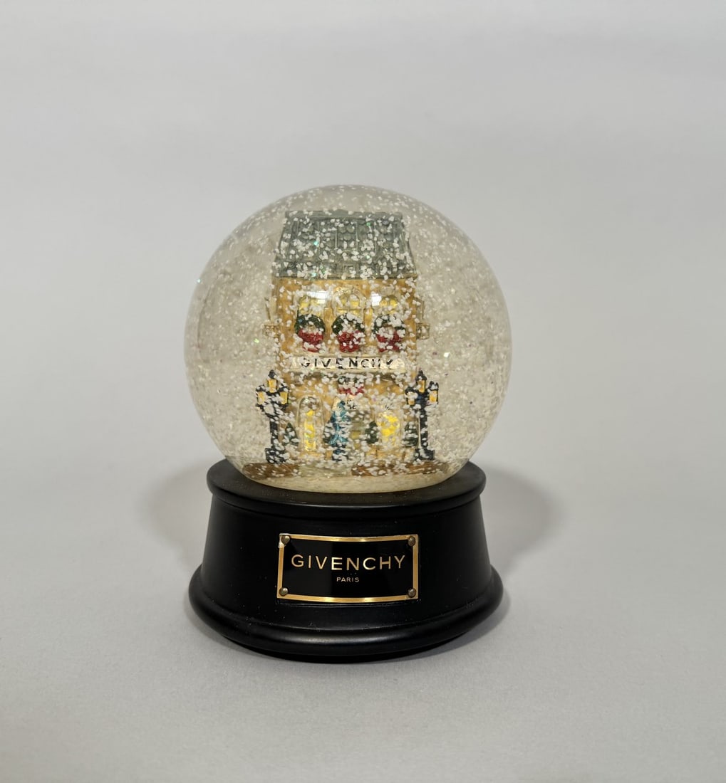 GIVENCHY.: GIVENCHY. Boule de neige musicale ornée de la boutique parisienne animée de personnages et d'une Rolls Royce. Hauteur : 15,5 cm.