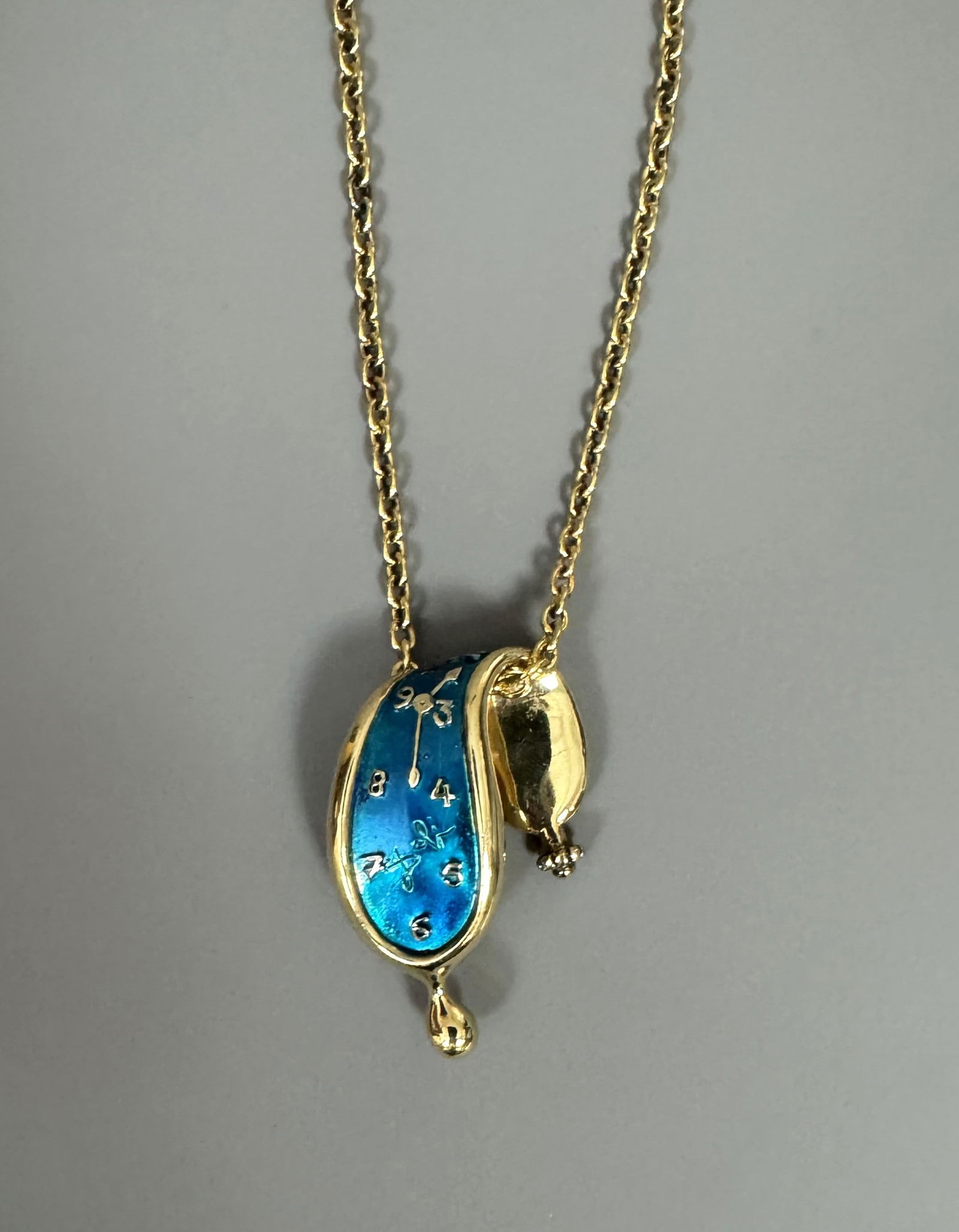 Salvador DALI (1904-1989). « Montre molle ». Circa 1980.: Salvador DALI (1904-1989). « Montre molle ». Circa 1980. Pendentif en argent doré émaillé bleu turquoise. Chaine en métal doré. Signé « Dali » sur le