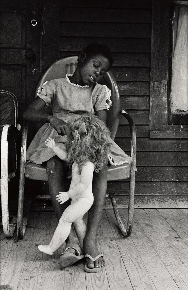 BRUCE DAVIDSON (1933- ) Child on a Front Porch Playing with her Doll Baby, Shelby County, Tennessee.: BRUCE DAVIDSON (1933- ) Child on a Front Porch Playing with her Doll Baby, Shelby County, Tennessee. Silver print, the image measuring 10x6¾ inches (25.4x17.1 cm.), the sheet 14x11 inches (35.6x2