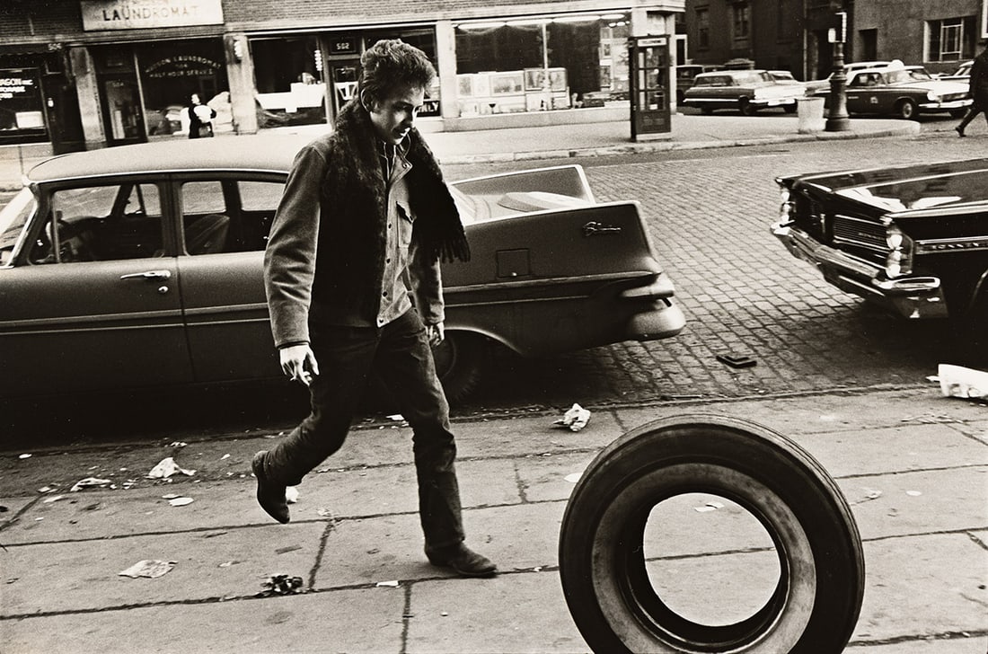 JIM MARSHALL (1936-2010) Bob Dylan Kicking Tire, New York City.: JIM MARSHALL (1936-2010) Bob Dylan Kicking Tire, New York City. Silver print, the image measuring 8x12 inches (20.3x30.5 cm.), the sheet 11x14 inches (27.9x35.6 cm.), the original mat 16x20 inches (40