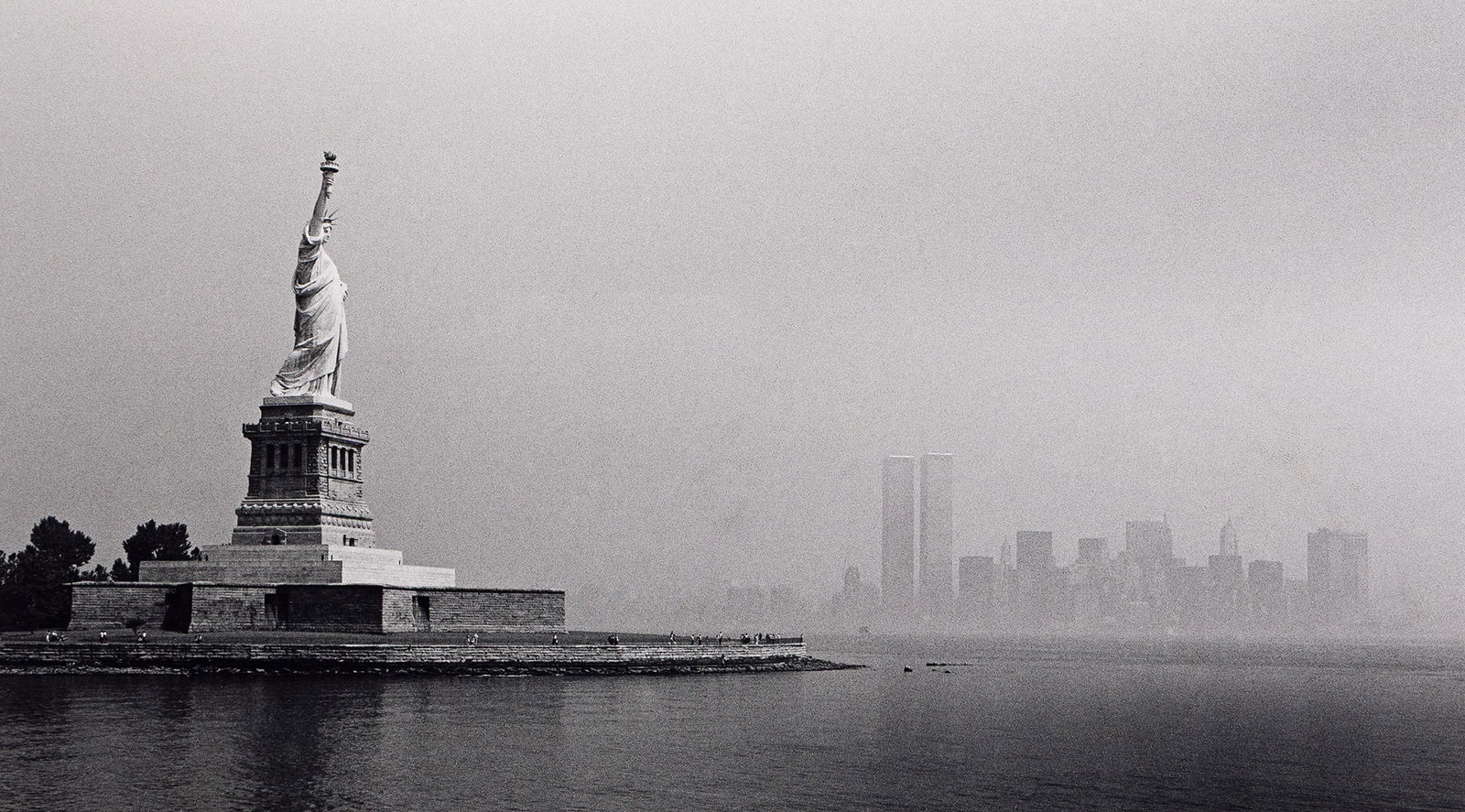George Forss, Statue of Liberty / City in Fog, 1978.: George Forss 1941-2021 Statue of Liberty / City in Fog. 1978. Silver print. With Forss' signature, title, and date with a stylus on print recto, and again in pencil on the overmat. The image 10 3/8 x 