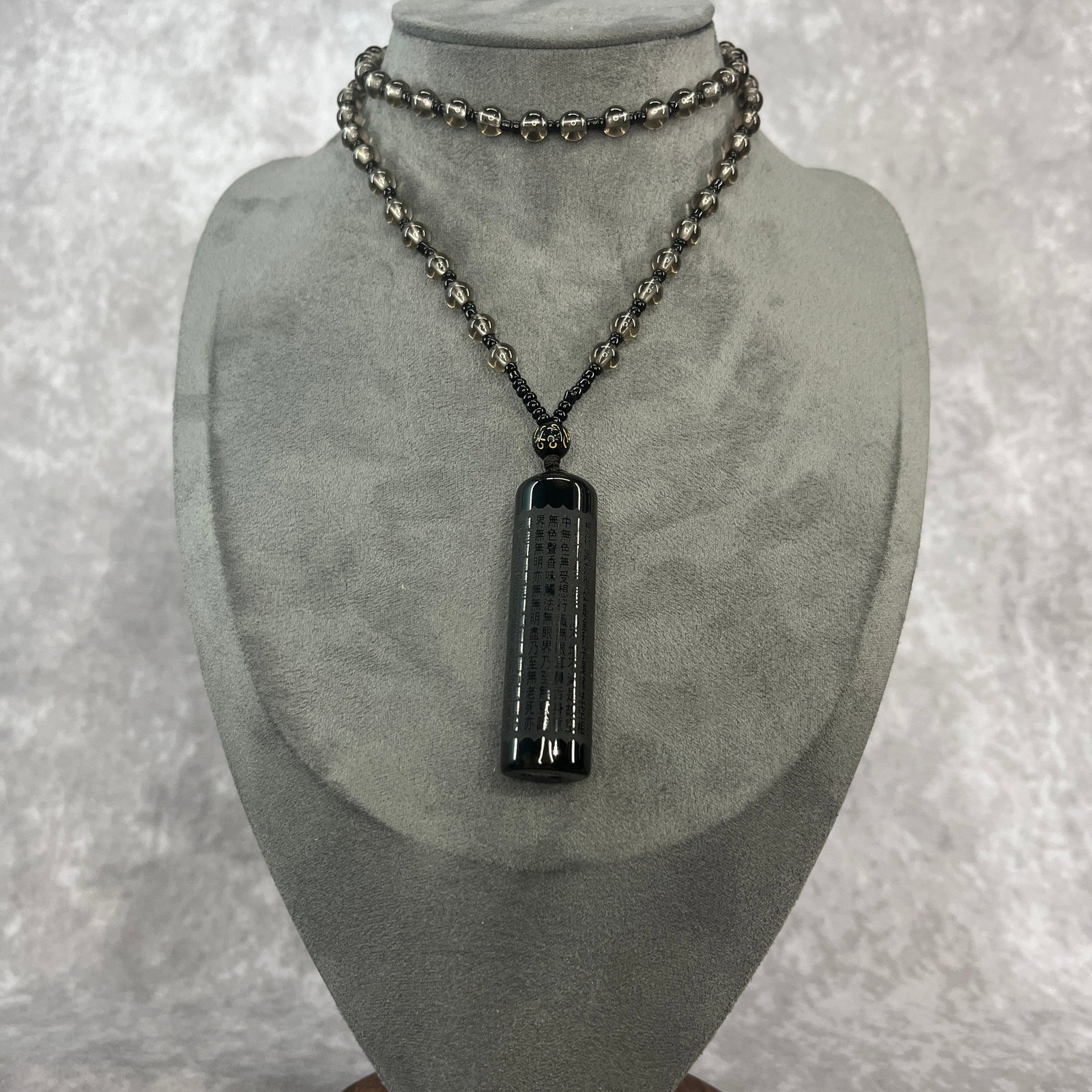 A FINE OBSIDIAN HEART SUTRA CYLINDER NECKLACE: Modern; Long: 2.38 inch; Diameter: 0.65 inch; Woodbase for picture and display only