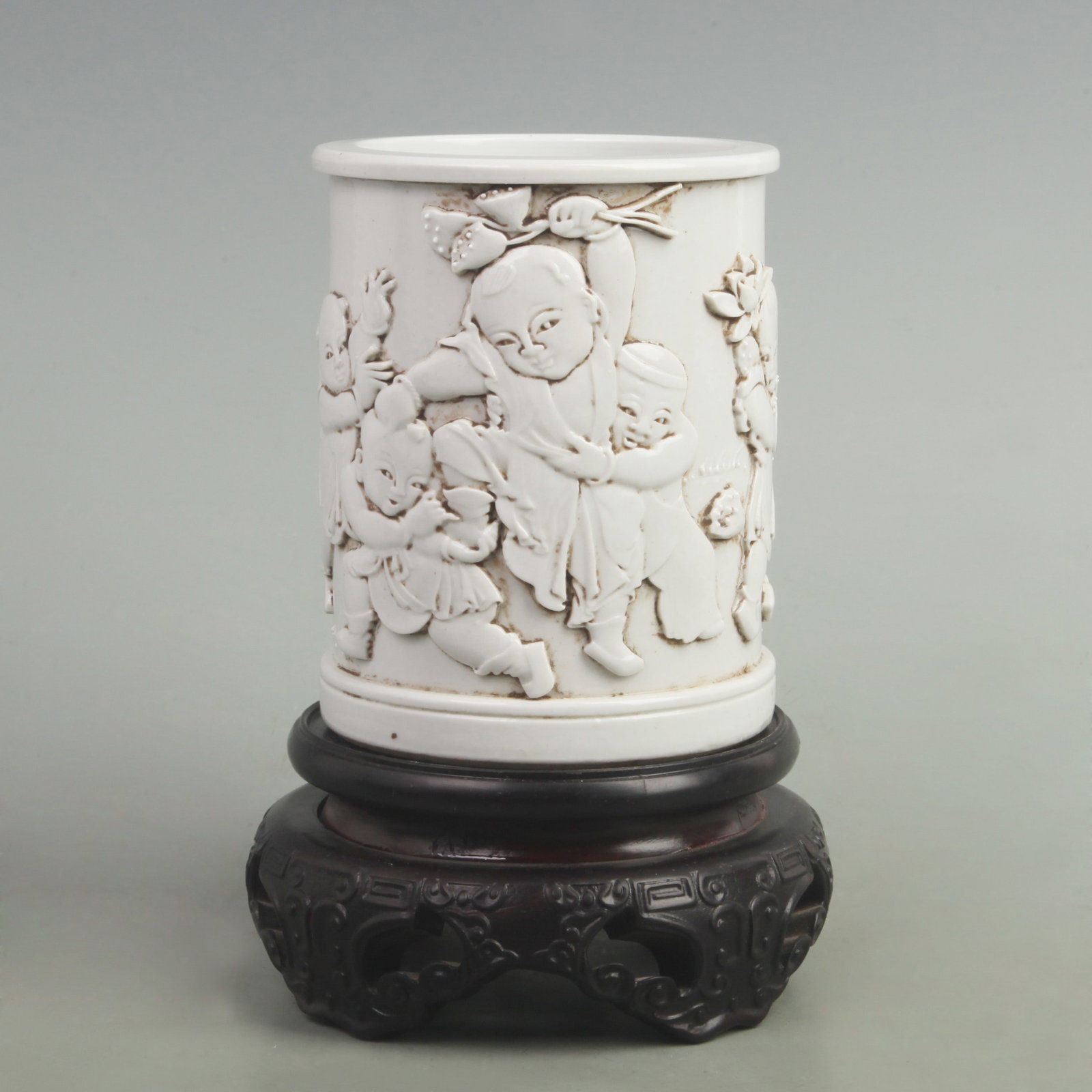 CARVED PORCELAIN BRUSH HOLDER WITH DEPICTION OF CHILDREN PLAYING: Qing Dynasty, High: 5.5 inch Diameter: 4.3 inch; Wooden base for picture and display only.