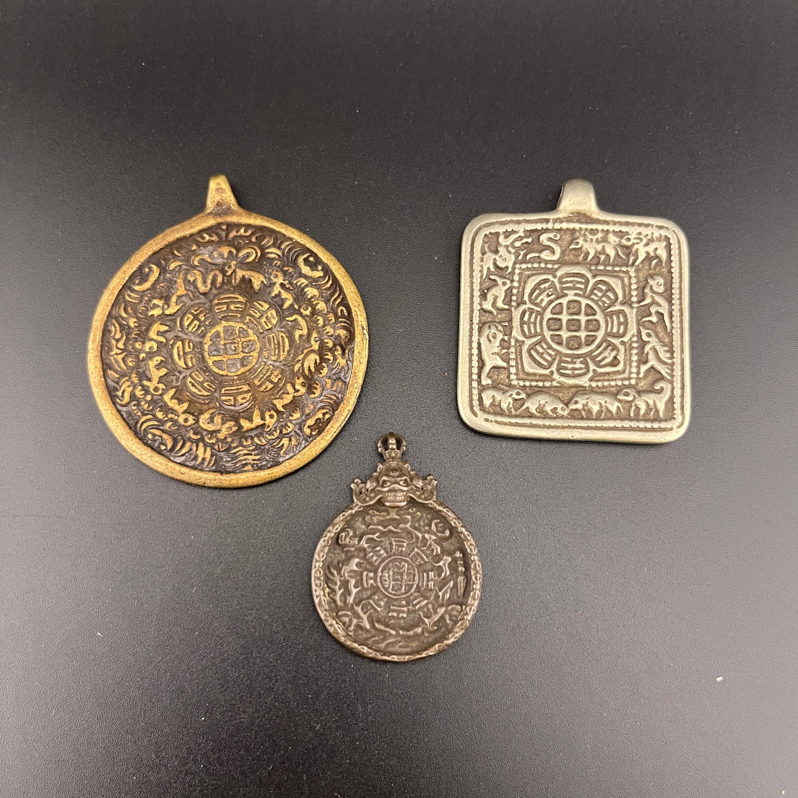 GROUP OF THREE TIBETAN ASTROLOGICAL AMULET PENDANTS SIPAHO PLAQUES: 20th Century; Long: 2.3 inch; Width: 1.95 inch; High: 0.18 inch; Long: 1.98 inch; Width: 1.65 inch; High: 0.2 inch; Long: 1.5 inch; Width: 1.13 inch; High: 0.2 inch; Woodbase for picture and display o
