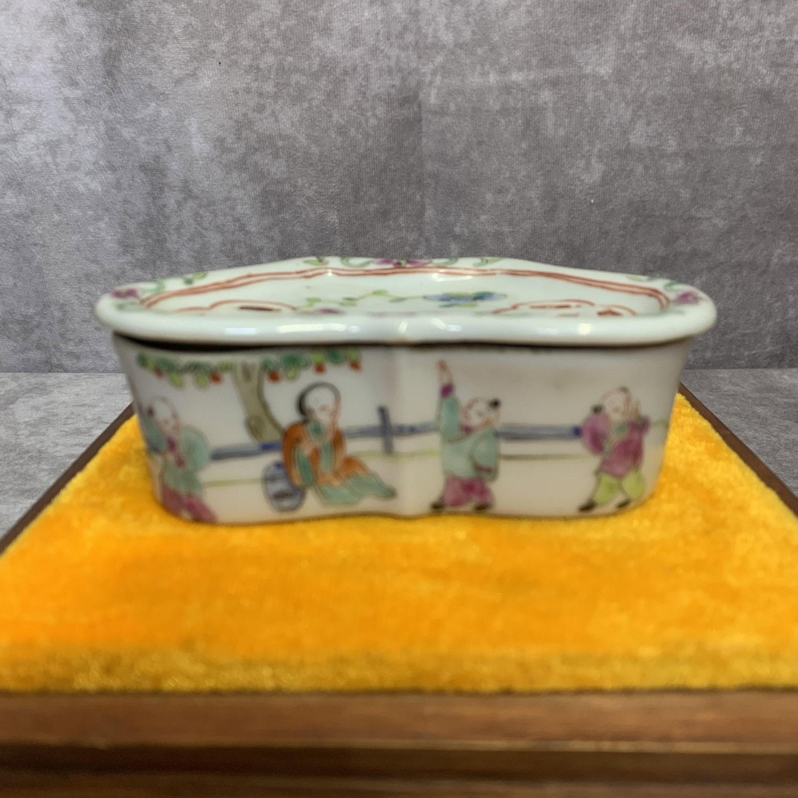 A SMALL FAMILLE ROSE BOY PLAYING PORCELAIN BOX: Qing Dynasty; High: 1.5 inch; Width: 2.3 inch; Diameter: 4.5 inch . Wooden base for display only