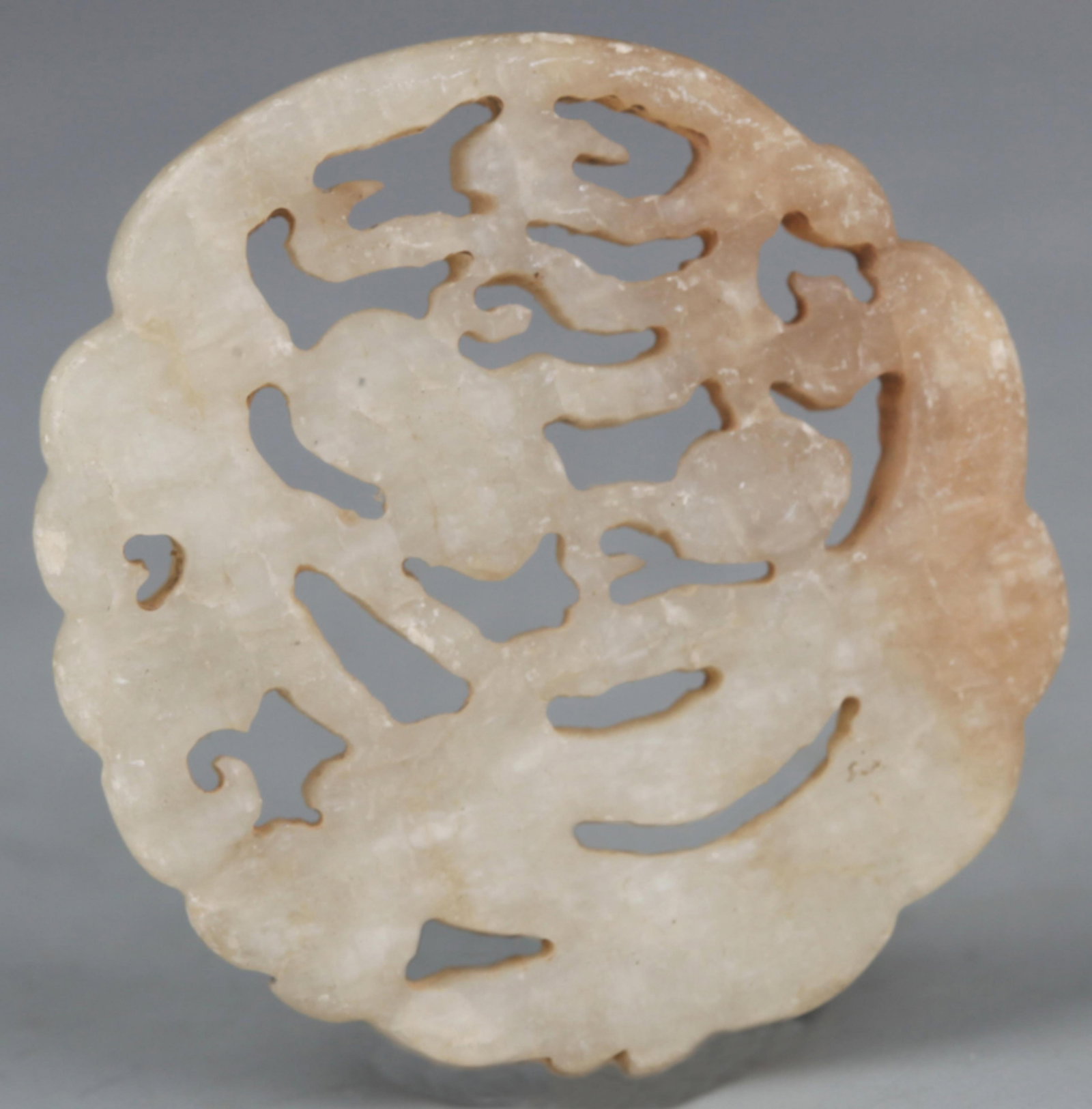 A FINELY CARVED PALE CELADON JADE PENDANT: 20th Century; Diameter: 1.65 inch; . Wooden base for display only