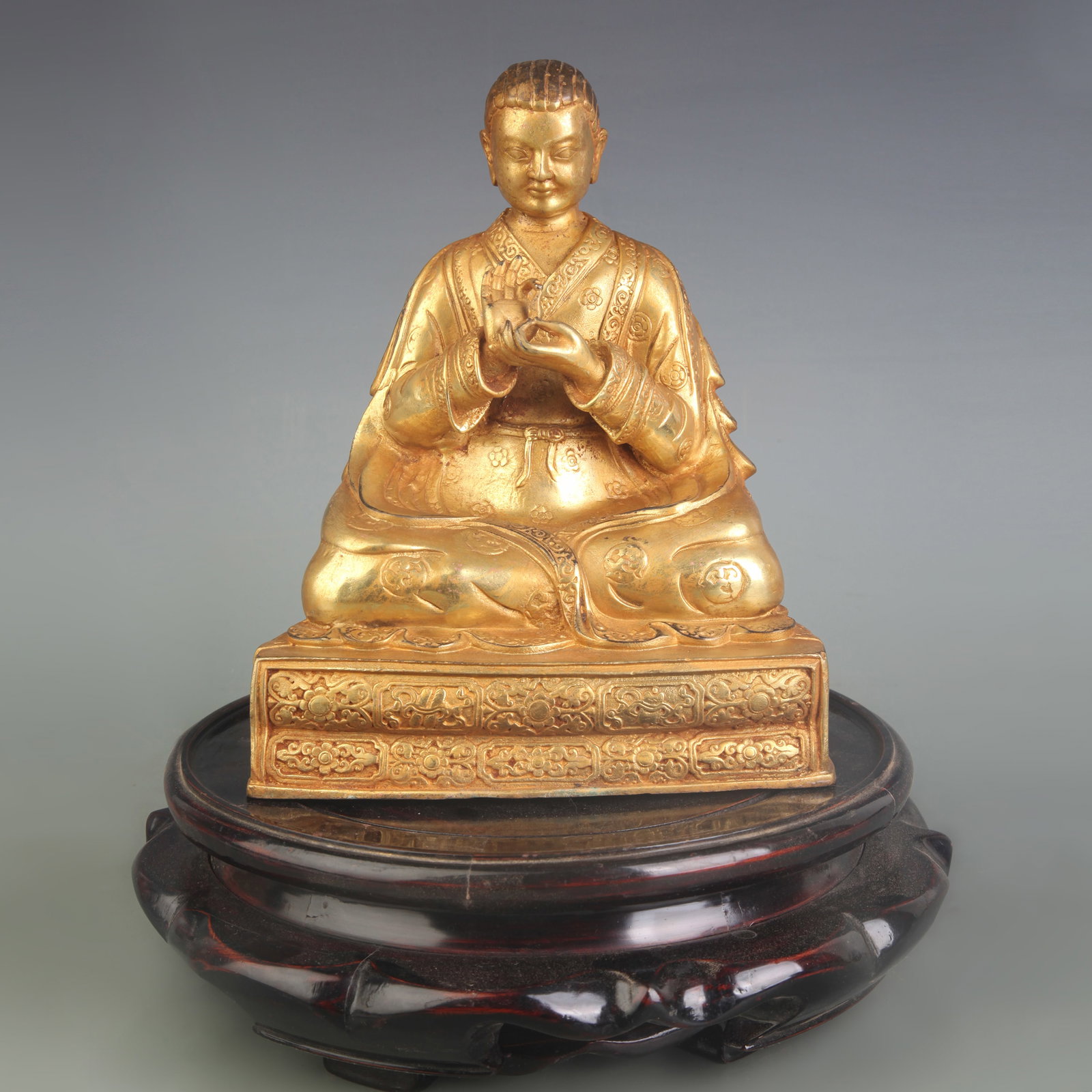 TIBETAN GILT BRONZE STATUE OF A SEATED LAMA: Qing Dynasty; W: 6.6 in ; High: 8.2 in. Wooden base for display only