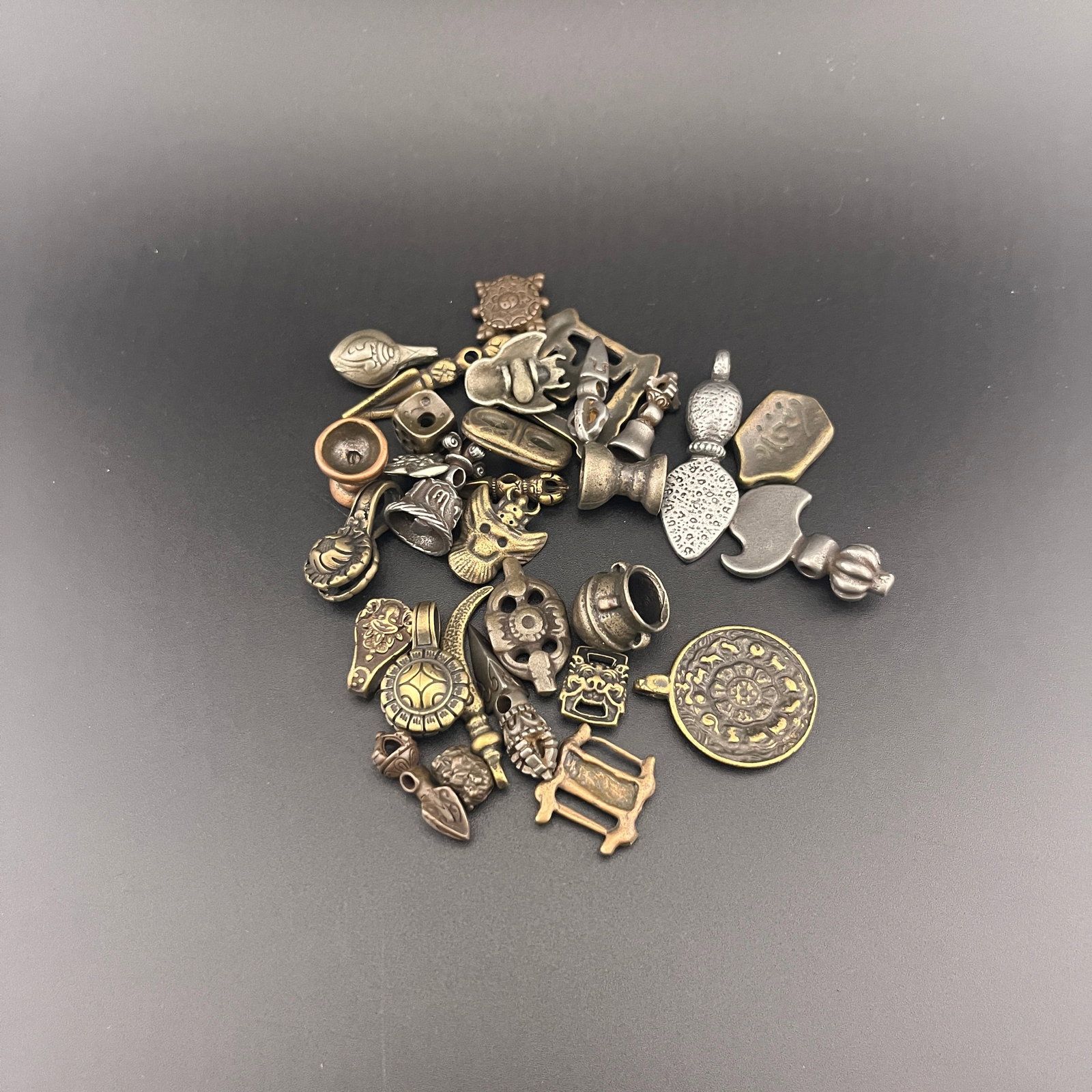 GROUP OF MINIATURE TIBETAN BRONZE THOGCHAG AMULETS: Long: 0.6 inch to 1.75 inch; Width: 0.52 inch to 0.6 inch; High: 0.13 inch to 0.38 inch; ;Wooden base for picture and display only.