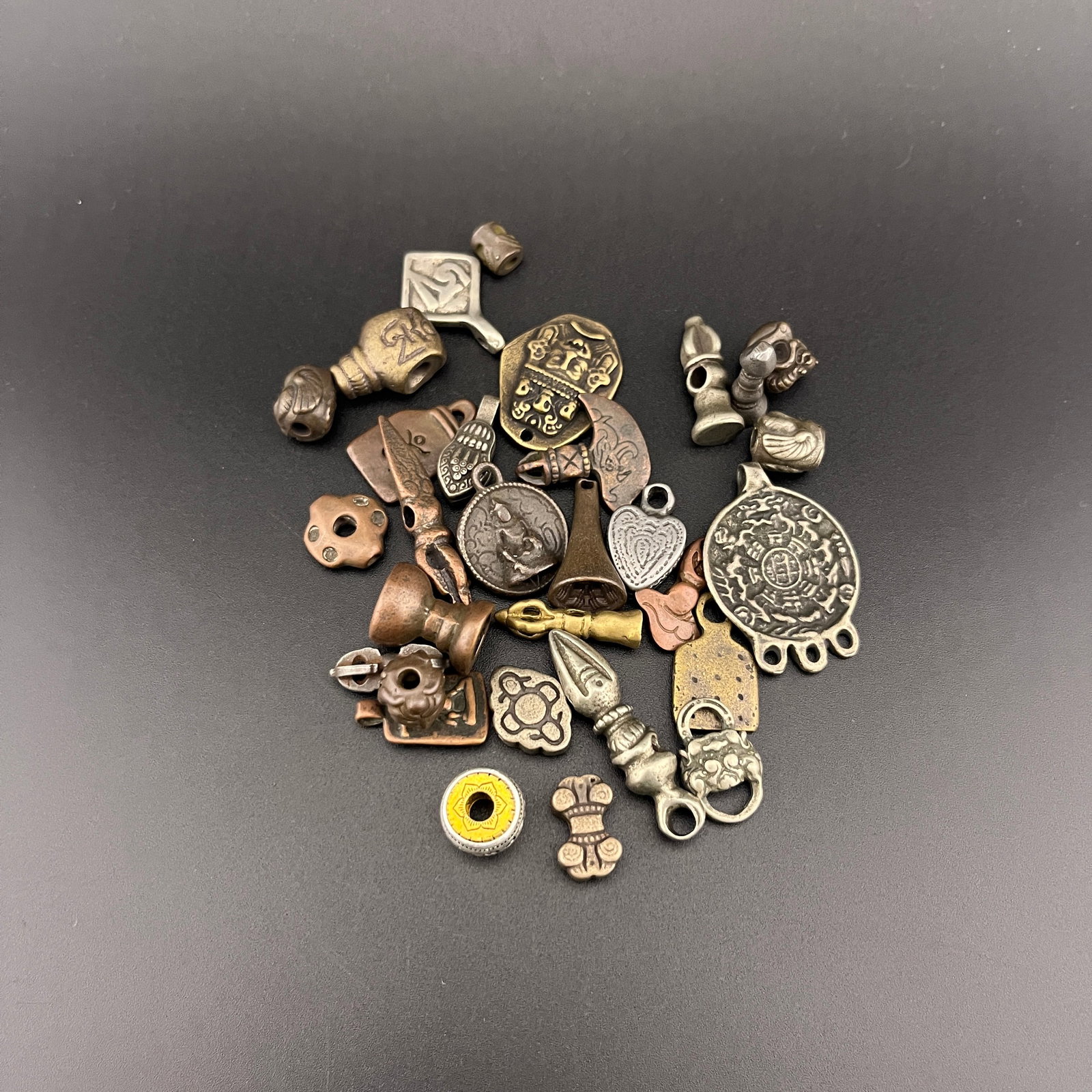 GROUP OF SMALL TIBETIAN AMULETS AND BEADS: Long: 0.4 inch to 1.36 inch; Width: 0.38 inch to 0.98 inch; High: 0.12 inch to 0.38 inch . Wooden base for display only