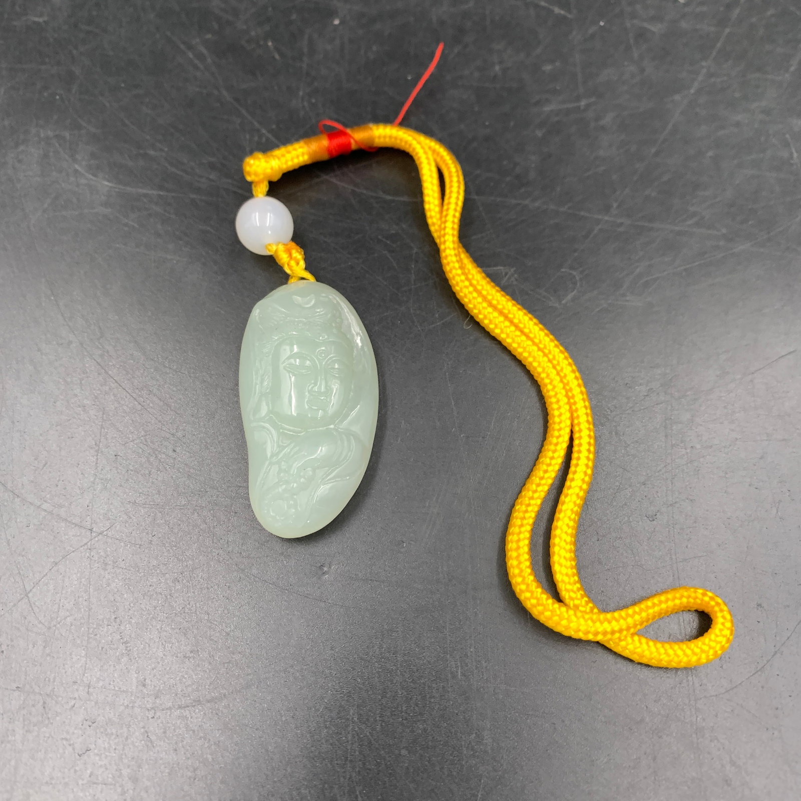 CARVED LIGHT-CELADON JADEITE "FACE OF GUANYIN" PEBBLE PENDANT