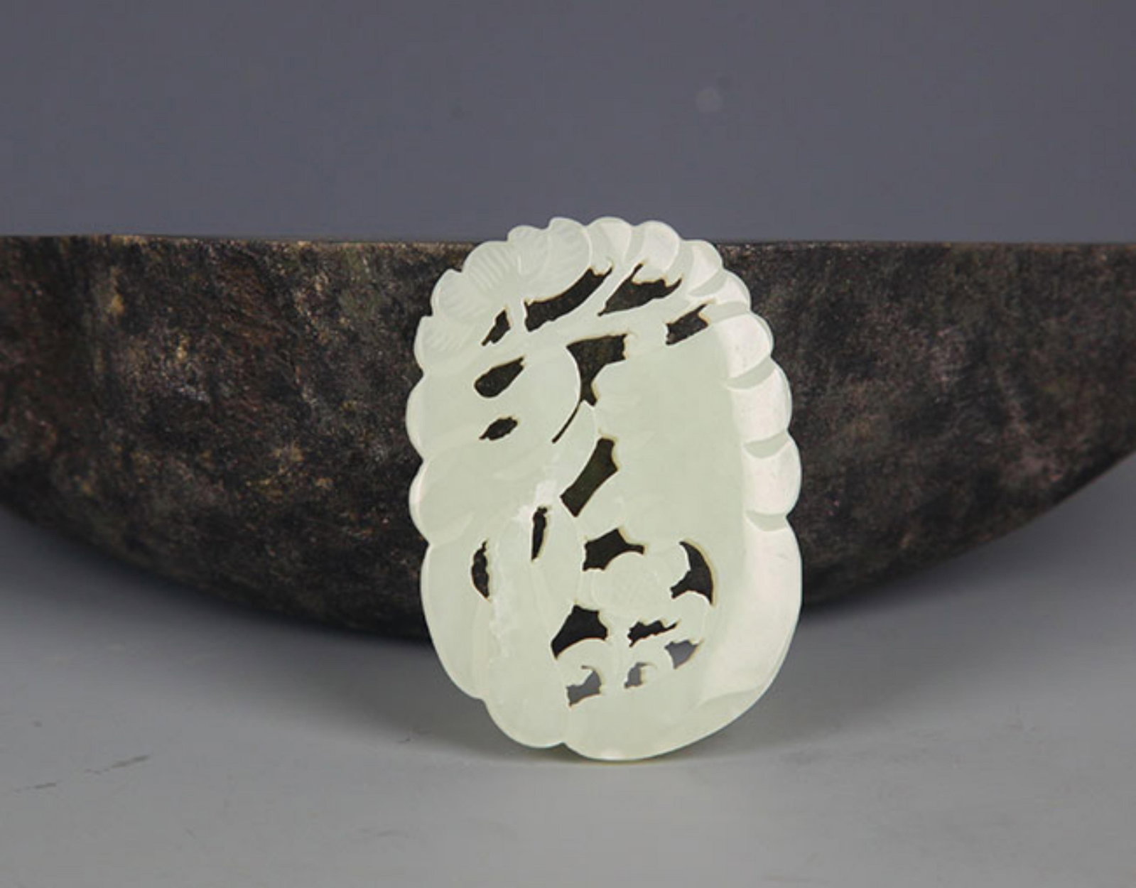 A FINELY CARVED HETIAN PALE CELADON JADE PENDANT PENDANT: Modern; High: 2.0 inch Width: 1.25 inch . Wooden base for display only