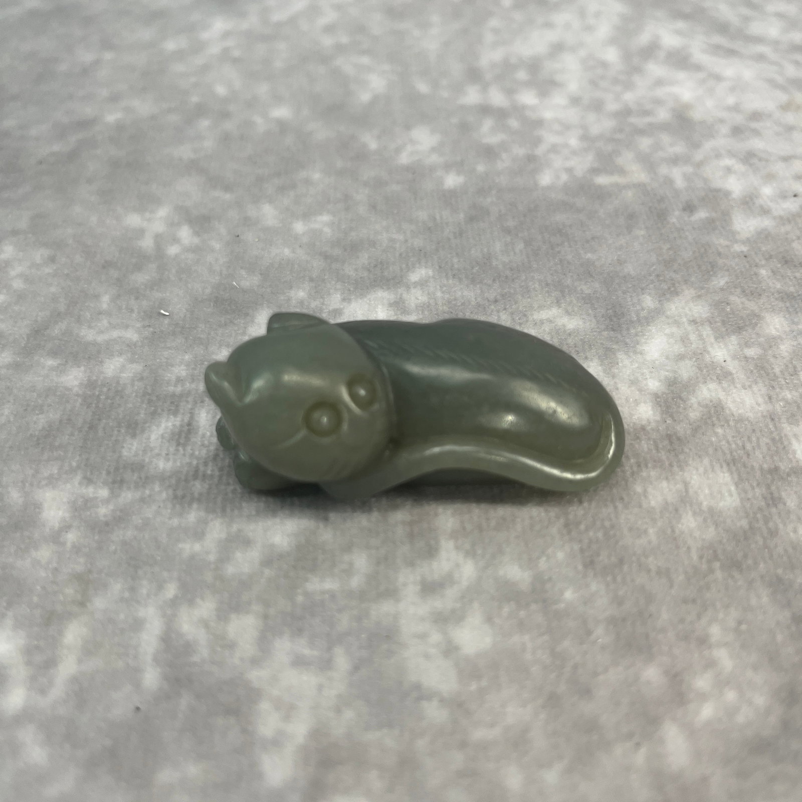 A CHINESE CARVED CELADON JADE FIGURE OF A RECUMBENT CAT OR KITTEN: Qing Dynasty; Long: 2.12 inch; Width:1.02 inch; High: 0.88 inch; wooden base for picture and display purpose only.