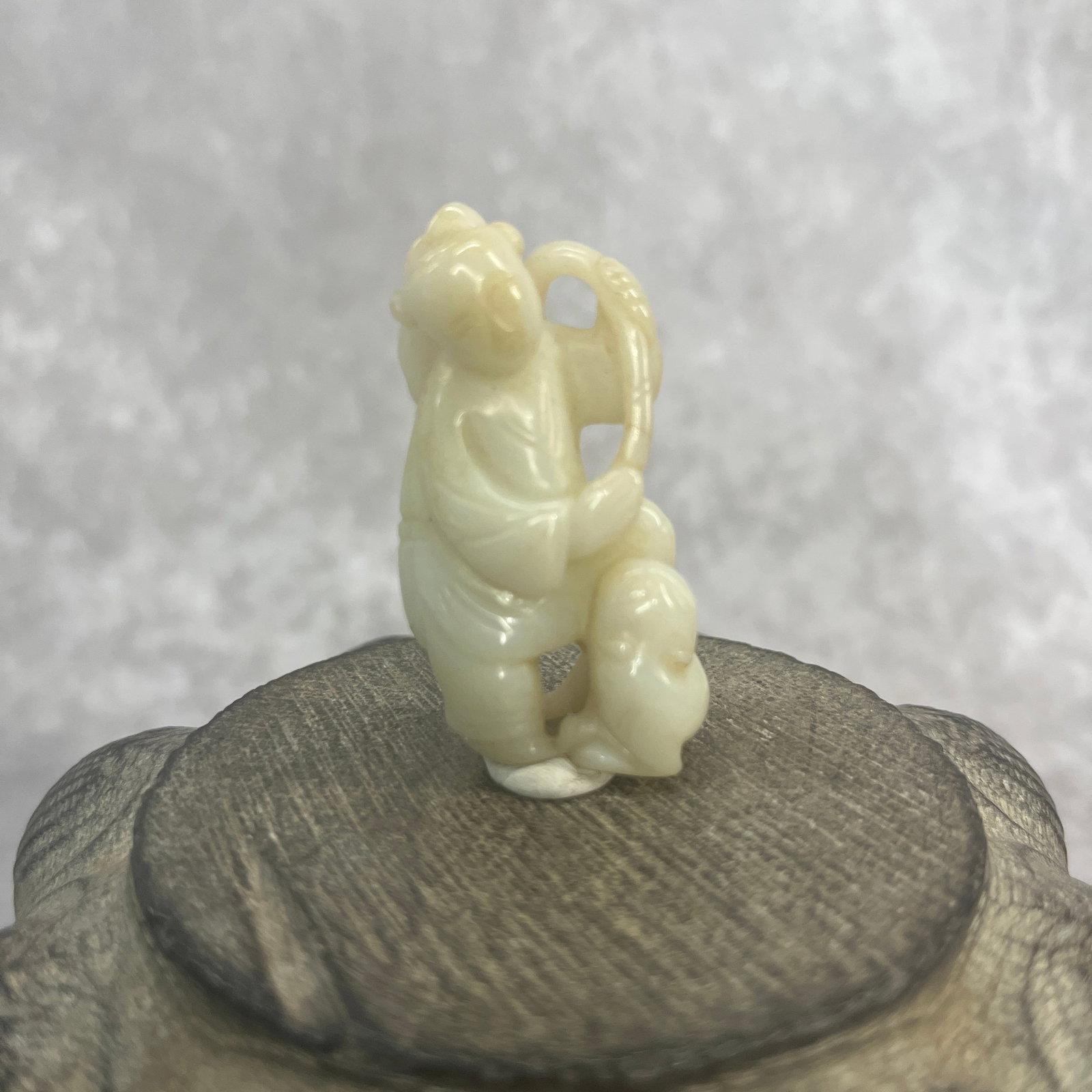 A FINE HETIAN PALE CELADON JADE IN FIGURE OF A BOY: Qing Dynasty; Long: 2.08 inch; Width: 1 inch; High: 0.6 inch; wooden base for picture and display purpose only.
