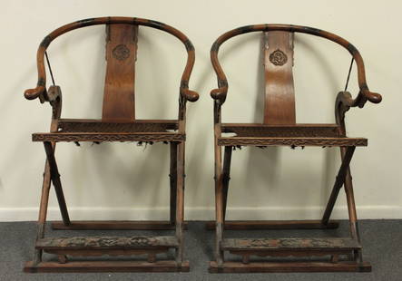 A PAIR OF HUANGHUALI HORSESHOE-BACK FOLDING ARMCHAIRS: 18th Century. Each has a rounded crest rail with scrolled arm ends, the vertical splat carved with a pair of dragons. The front legs curve up and extend forward to support the crest rail with metal