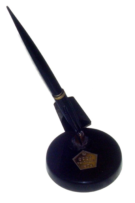 1959 Luna 1 Commemorative Fountain Pen & Holder: A striking black plastic fountain pen mounted in a "rocket" shaped holder with a 3.5" round plastic base. There is a golden band on the pen and a golden pentagonal plaque on the base that reads: "The 