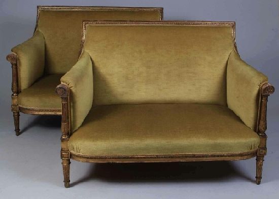 A pair of french gilded settees, each with carved: A pair of french gilded settees, each with carved square backs, with scroll and floral roundel above reeded columns, raised on short reeded supports