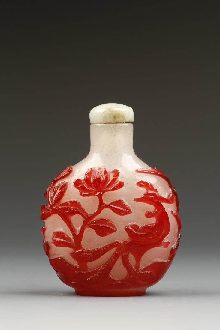 A RED-OVERLAID GLASS SNUFF BOTTLE of rounded form carve: A RED-OVERLAID GLASS SNUFF BOTTLE of rounded form carved with a phoenix among blossoming flowers, 1880-1910, hardstone stopper, 3" high Provenance: The Anthony Bate Collection of Chinese Snuff Bottles