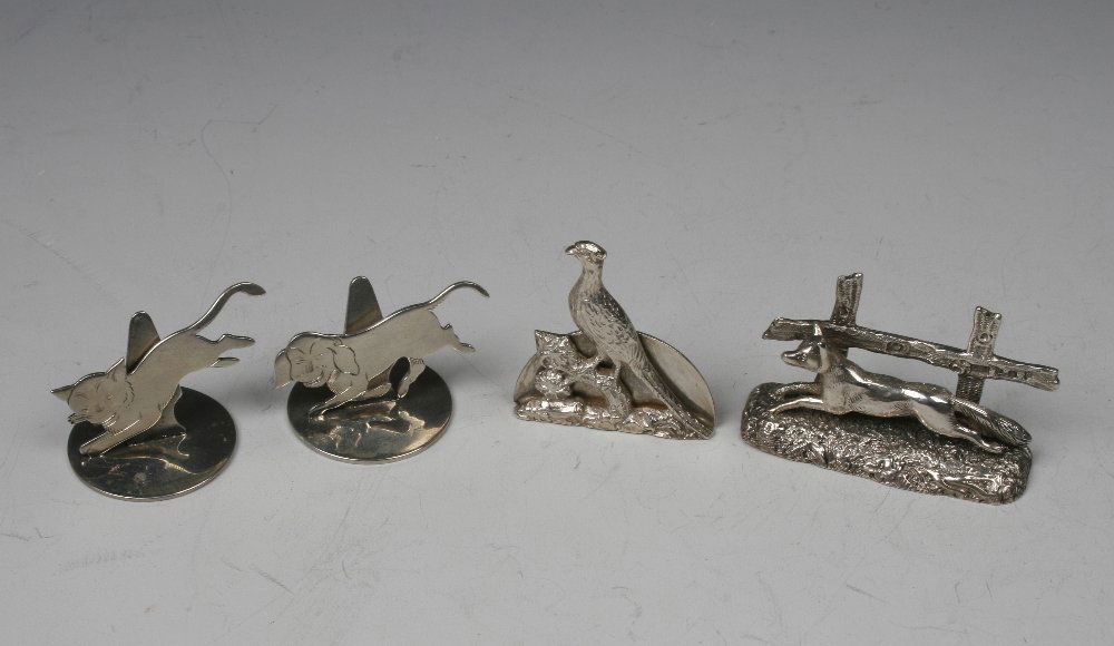 A PAIR OF MENU CARD HOLDERS modelled in the form of a r: A PAIR OF MENU CARD HOLDERS modelled in the form of a running dog and a running cat, by Sampson Mordan & Co., London 1925, 1.25" high, a running fox in front of a fence and another (4)¦