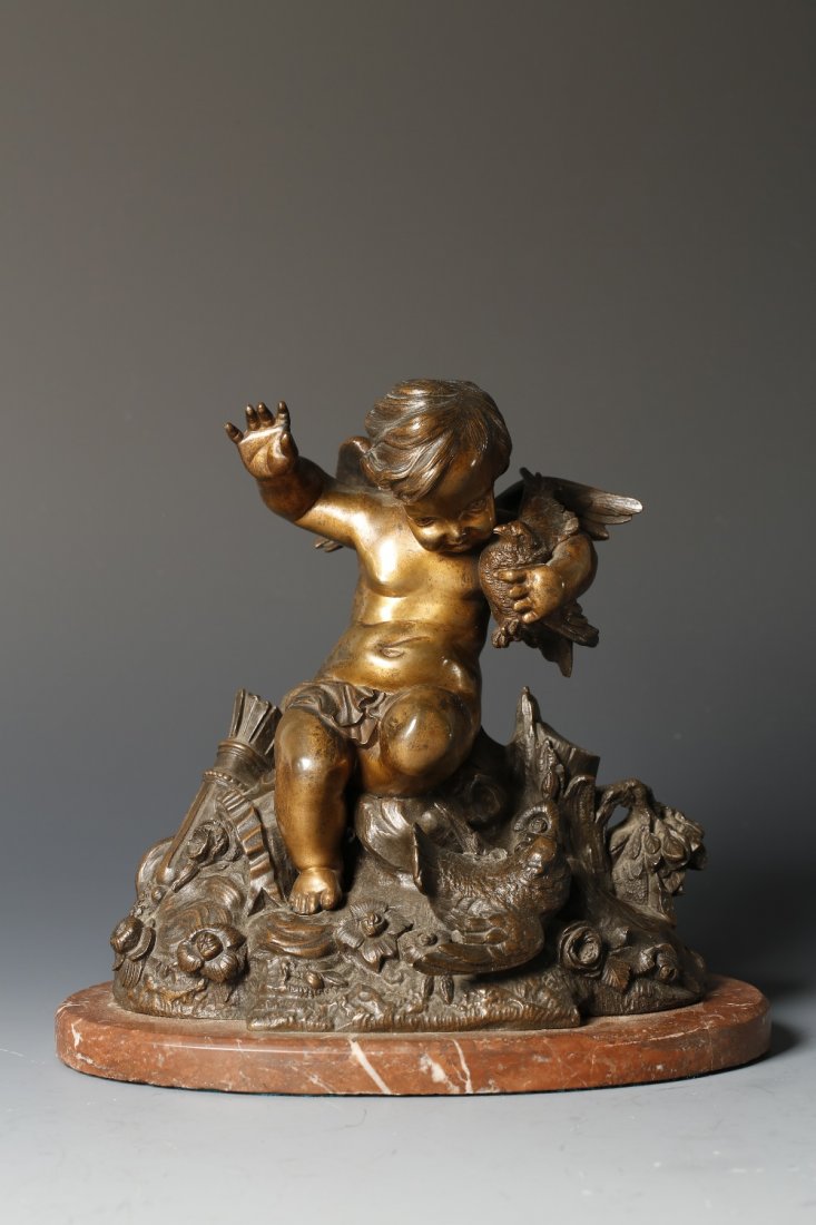 A CAST AND PATINATED BRONZE SCULPTURE in the manner of : A CAST AND PATINATED BRONZE SCULPTURE in the manner of Claude Clodion of a winged cherub holding a staff, on a naturalistic base and marble stand, 8" wide