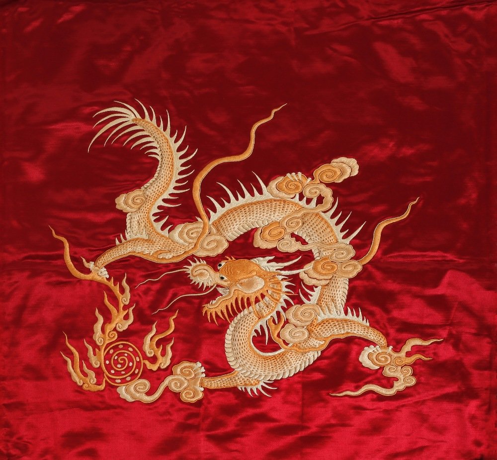 TWO SIMILAR EMBROIDERED DRAGON PANELS, one with a: TWO SIMILAR EMBROIDERED DRAGON PANELS, one with a curled dragon chasing a flaming pearl amongst clouds, on a ruby ground, the other with a similar four-clawed dragon, on a yellow ground, late 19th/ear