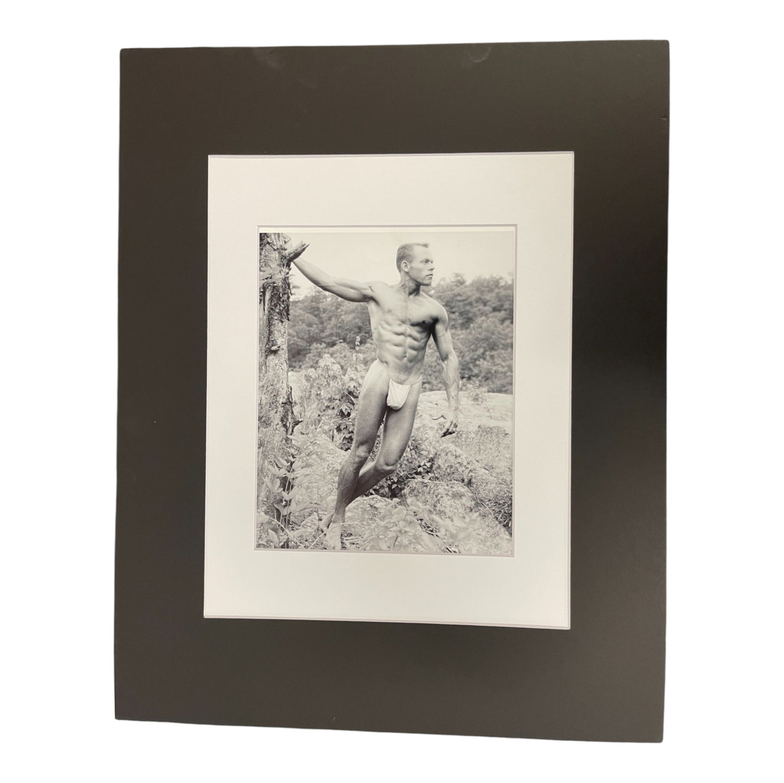 Vintage Male Physique Photograph Outdoor Pose: Black and white vintage male physique photograph of a muscular man posing outdoors in nature, wearing a posing brief. Circa 1950s1960s, classic physique photography style. Matted and preserved.
