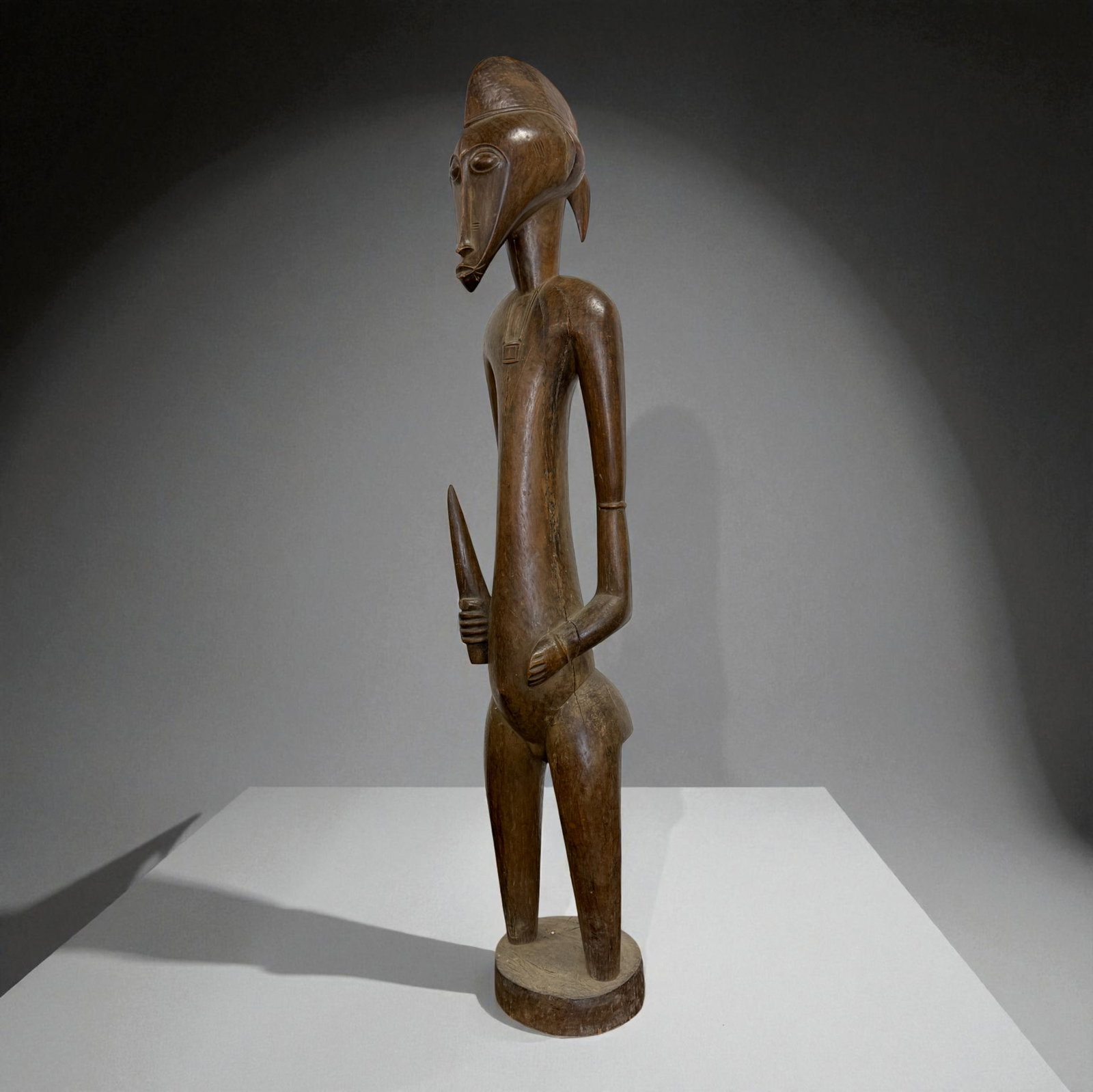 African Carved Male Figure: Tall elongated wooden male figure with stylized facial mask features and spear-like form. 19th–20th Century tribal carving. Provenance: Beverly Hills Barakat Gallery Collection. 41" inches