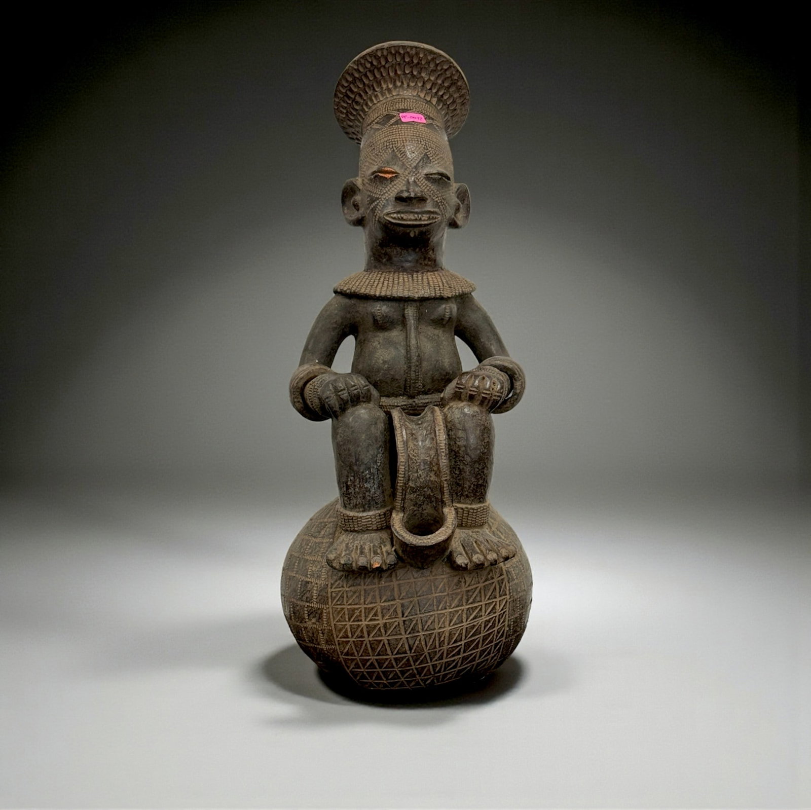 African Carved Male Figure: Carved wooden seated figure atop a spherical base, wearing a detailed headdress and jewelry patterns, representing prestige iconography. 19th–20th Century. Provenance: Beverly Hills Barakat Gallery 