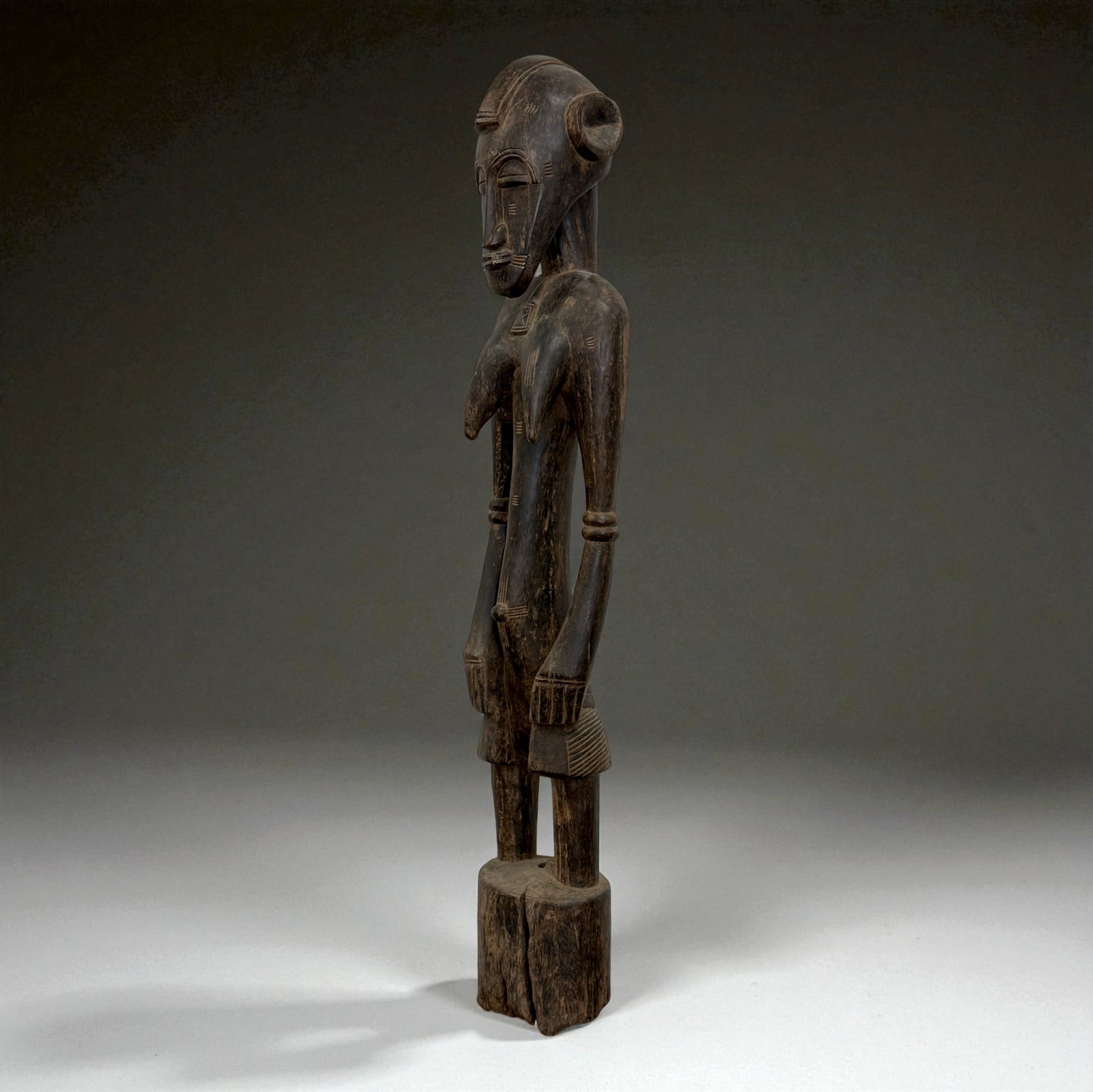 African Carved Male Figure: Slender wooden male figure with high crested hairstyle, elongated torso, and traditional arm bracelets. 19th–20th Century. Provenance: Beverly Hills Barakat Gallery Collection. 36" inches
