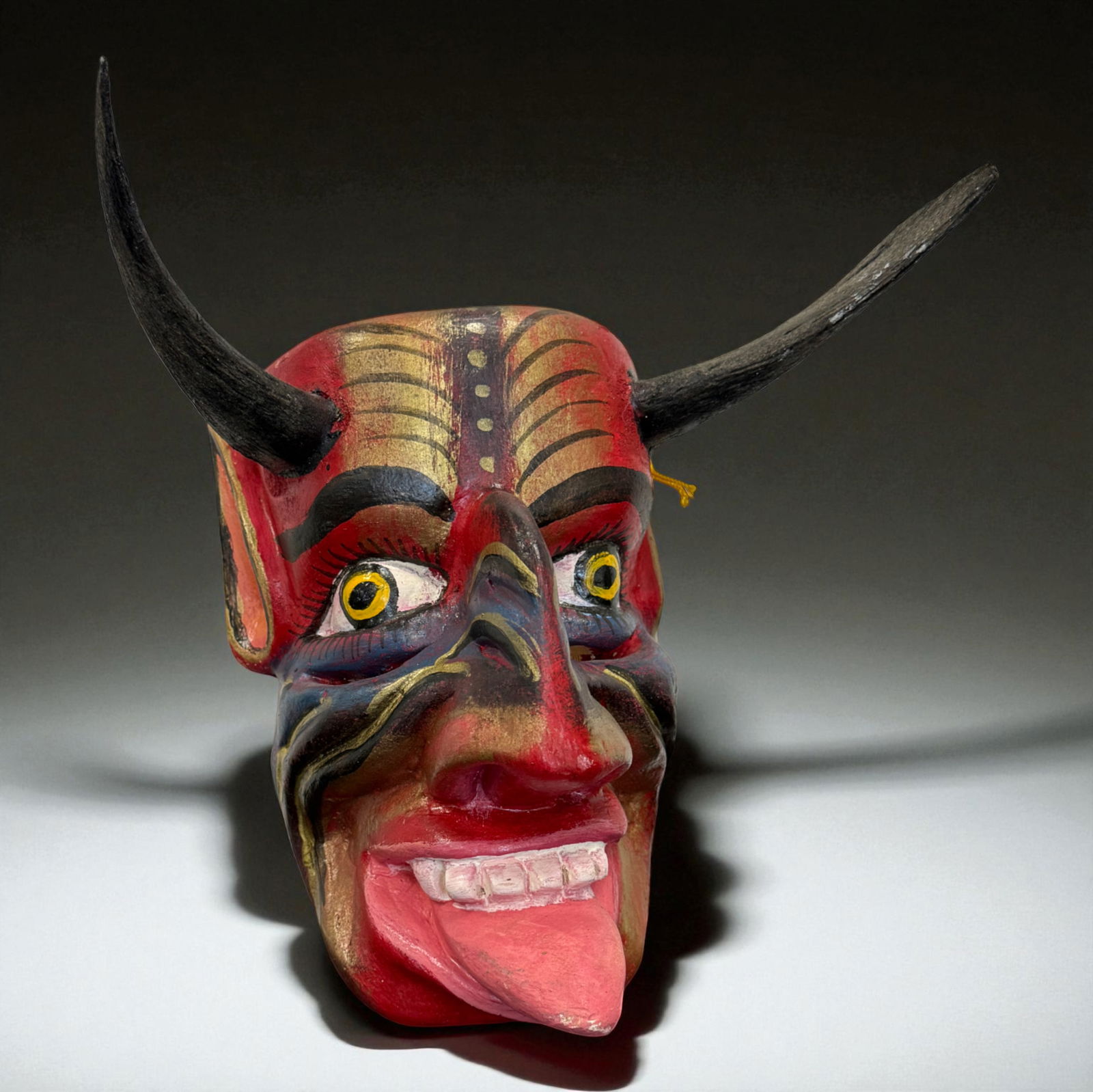 African Polychrome Devil Dance Mask: African carved wooden “devil” dance mask with horns, bulging yellow-rimmed eyes, exaggerated red nose and tongue, and multi-colored painted details; lively theatrical presence with evident use