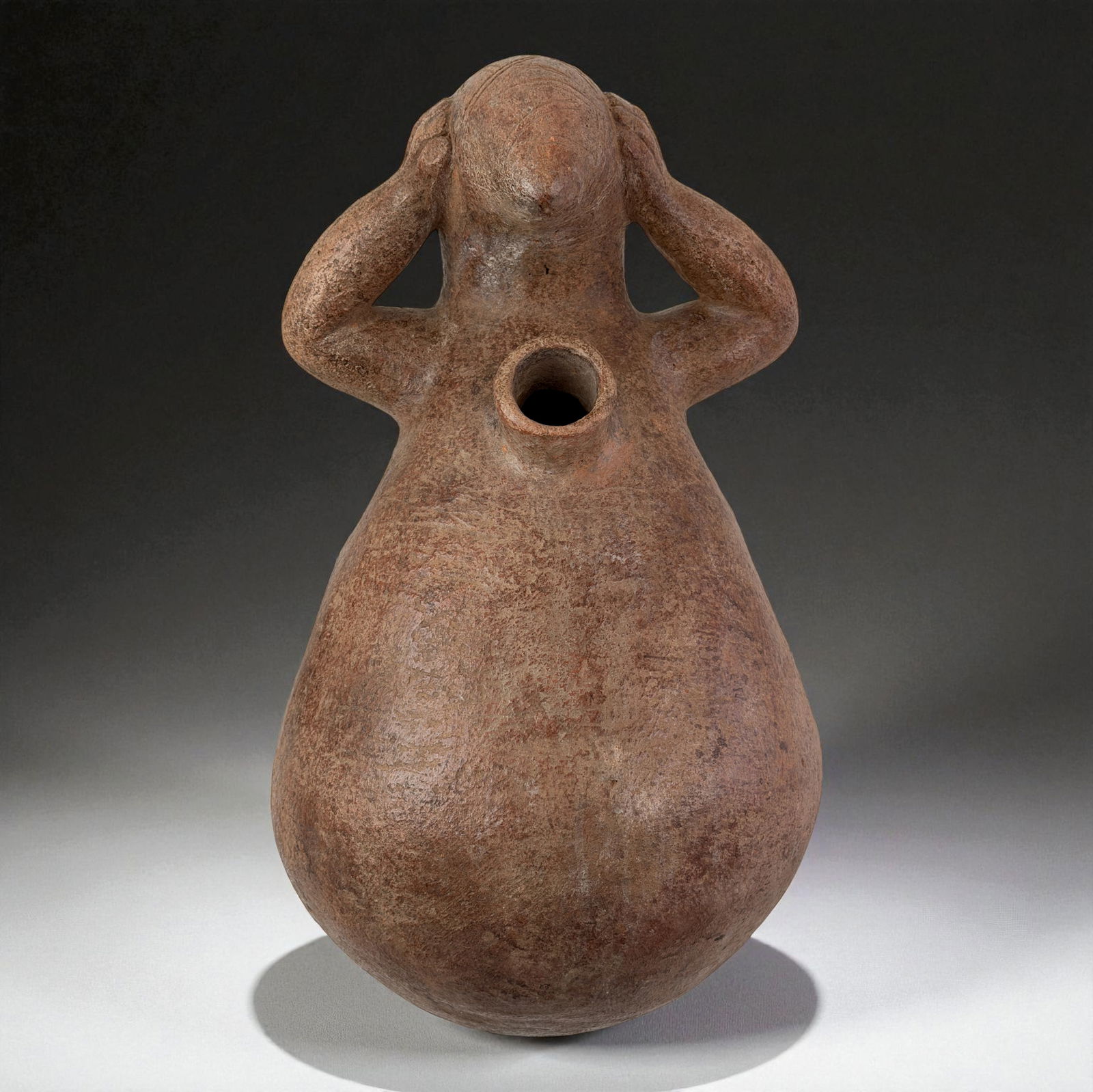 Pre-Columbian Effigy Vessel With Opening: Abstract ceramic effigy with smooth rounded body and a circular chest opening, possibly used for ritual pouring or offerings. Simplified human form with hands raised to the head, rendered in natural c