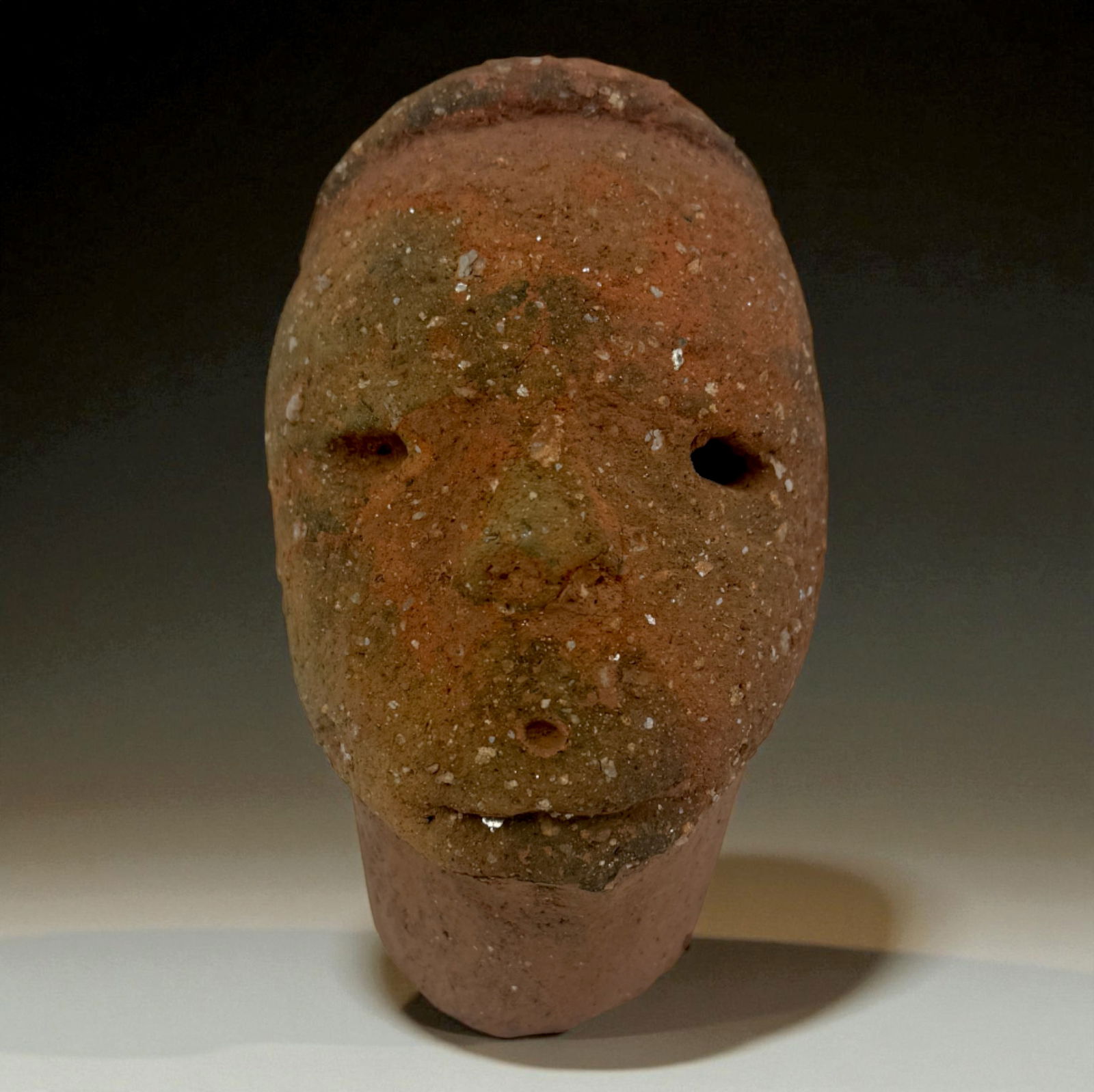 Pre-Columbian Terracotta Mask Fragment: Carved terracotta mask fragment with simple eye openings, pronounced brow, and earthy red-brown pigmentation. Subtle mineral accretions and weathering consistent with antiquity. A powerful minimalist