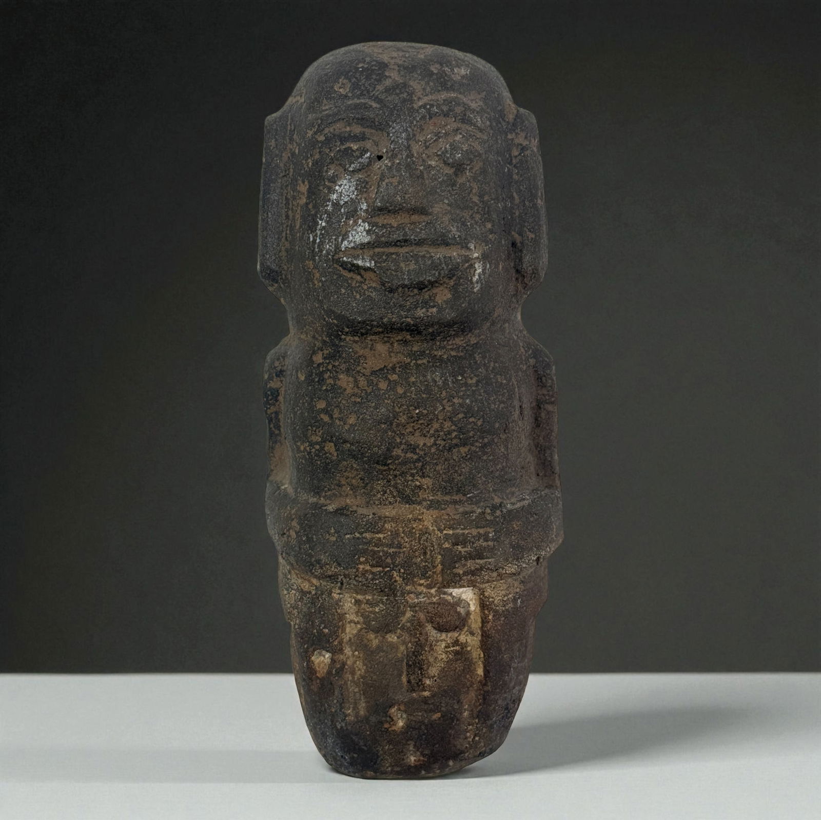 Pre-Columbian Stone Figure Fragment: Dark stone carved figure with prominent facial features, compact torso, and mineral deposits across the surface. Strong sculptural weight and bold expression, retaining deep cultural character. Proven