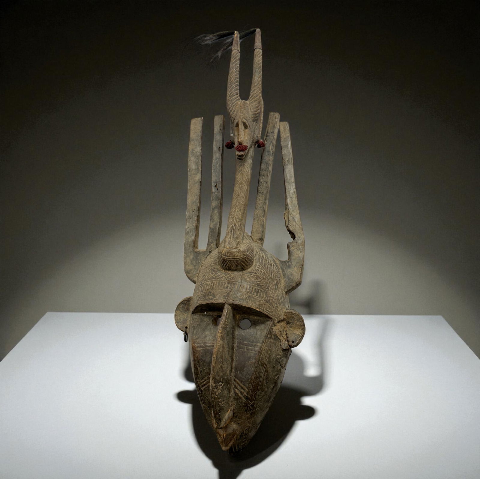 African Tall Crest Helmet Mask: African helmet-style mask carved with an elongated face and high vertical crest rising from the crown, flanked by upright forked elements and geometric incising; old surface with areas of wear and min