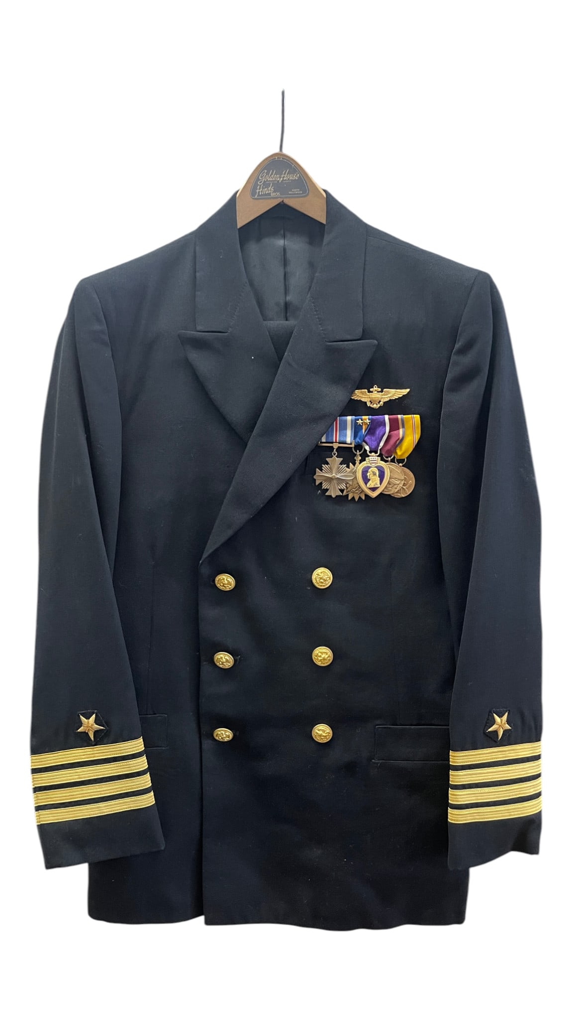 U.S. Naval Officer Dress Uniform Jacket with Medals: Dark navy double-breasted naval officer’s dress jacket with gold buttons, rank striping at the cuffs, officer stars, aviation-style insignia, and mounted medal group including a Purple Heart. A
