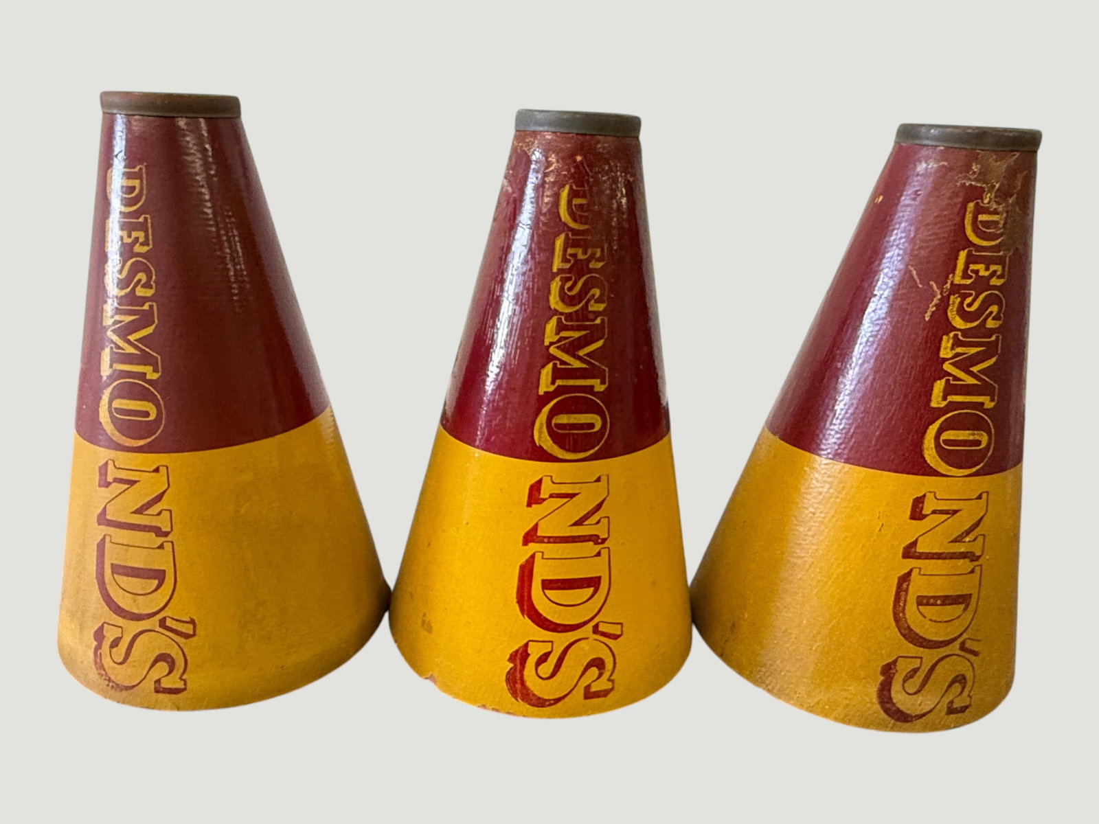 Set of 3 Vintage Desmond's Department Store Promotional Megaphones: A matched set of three vintage cardboard cheerleader-style megaphones bearing the 'Desmond's' branding in bold lettering, finished in the classic Desmond's maroon and gold color scheme. Desmond's was 