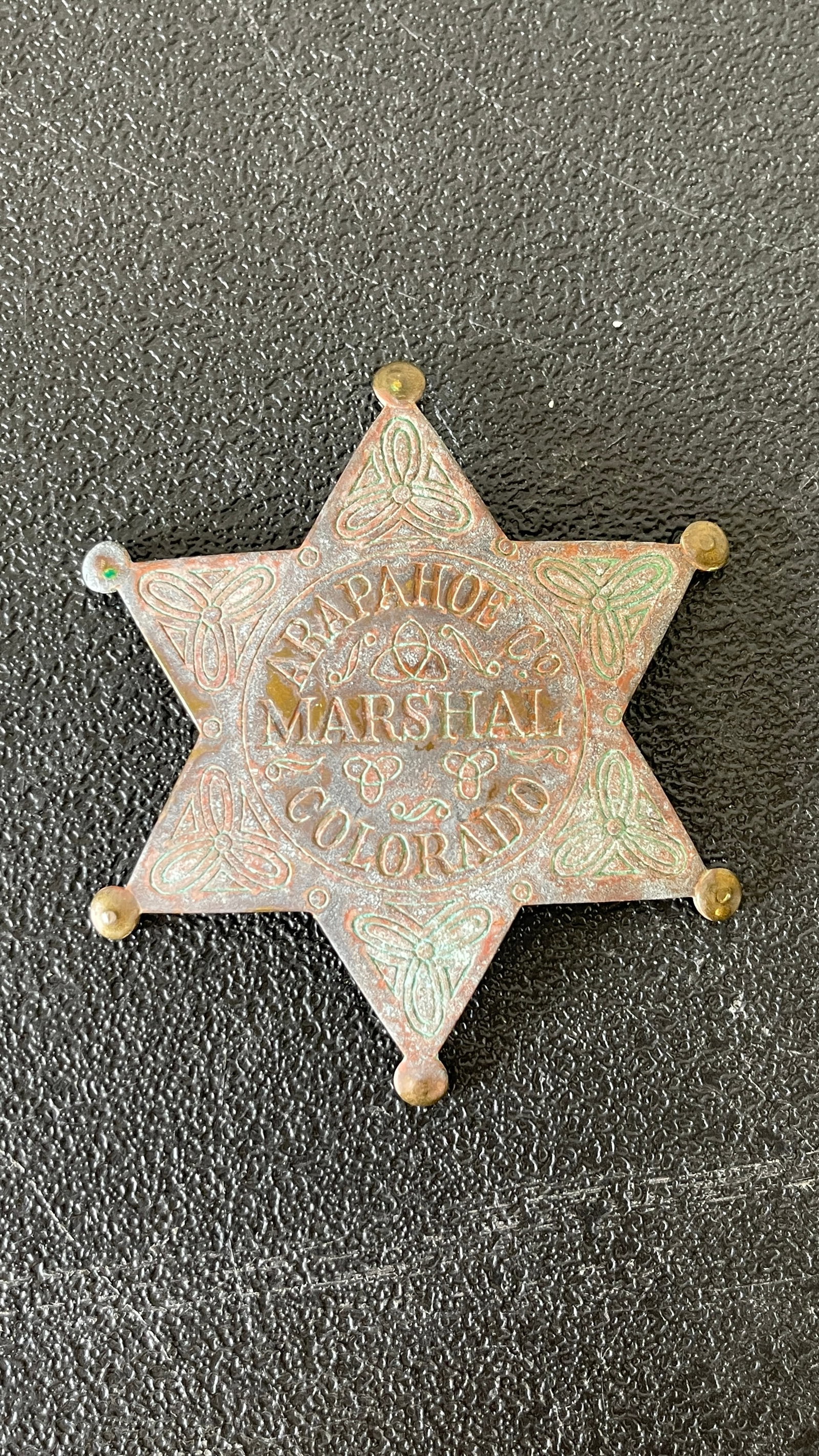 Arapahoe County Marshal Colorado Six-Point Star Badge, Brass, Old West Era: A six-pointed star lawman's badge reading 'Arapahoe Co. Marshal Colorado,' crafted from brass with decorative Celtic-style knotwork engravings on each point and a raised central cartouche with the tex