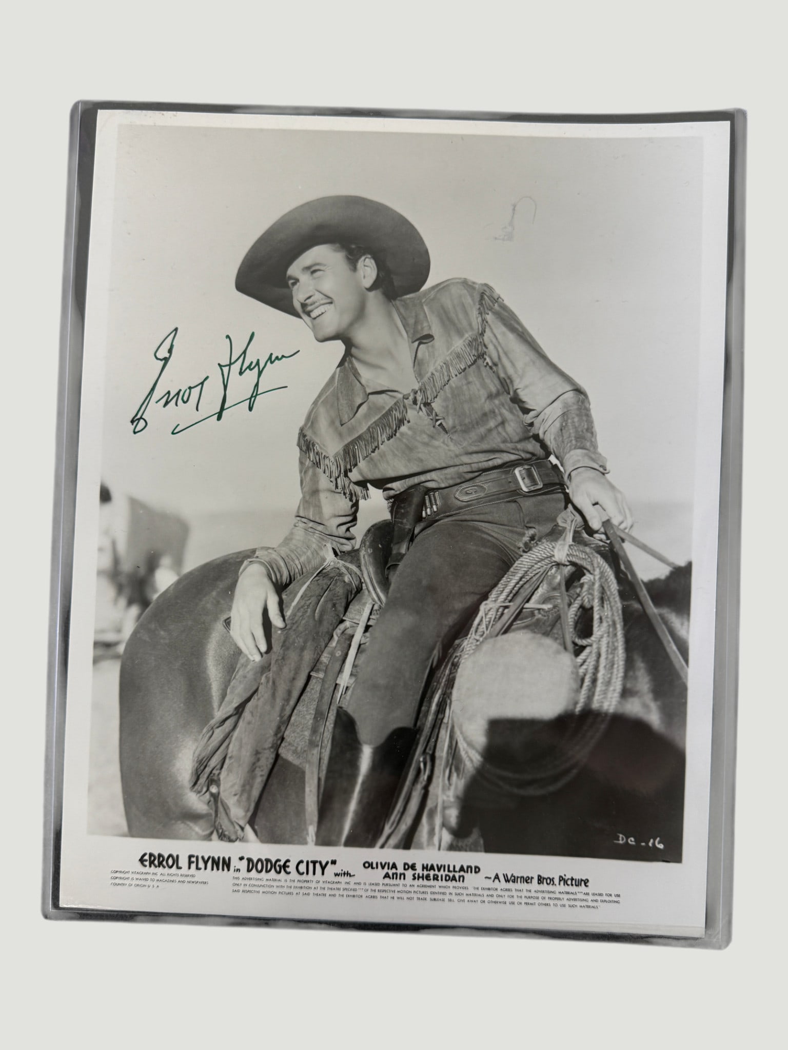 Errol Flynn Signed 8x10 Promo Photo – 'Dodge City' (1939) Warner Bros.: An original Warner Bros. promotional still photograph from the 1939 western 'Dodge City,' featuring Errol Flynn in full cowboy attire on horseback. The photo bears a bold ink autograph reading 'Errol 