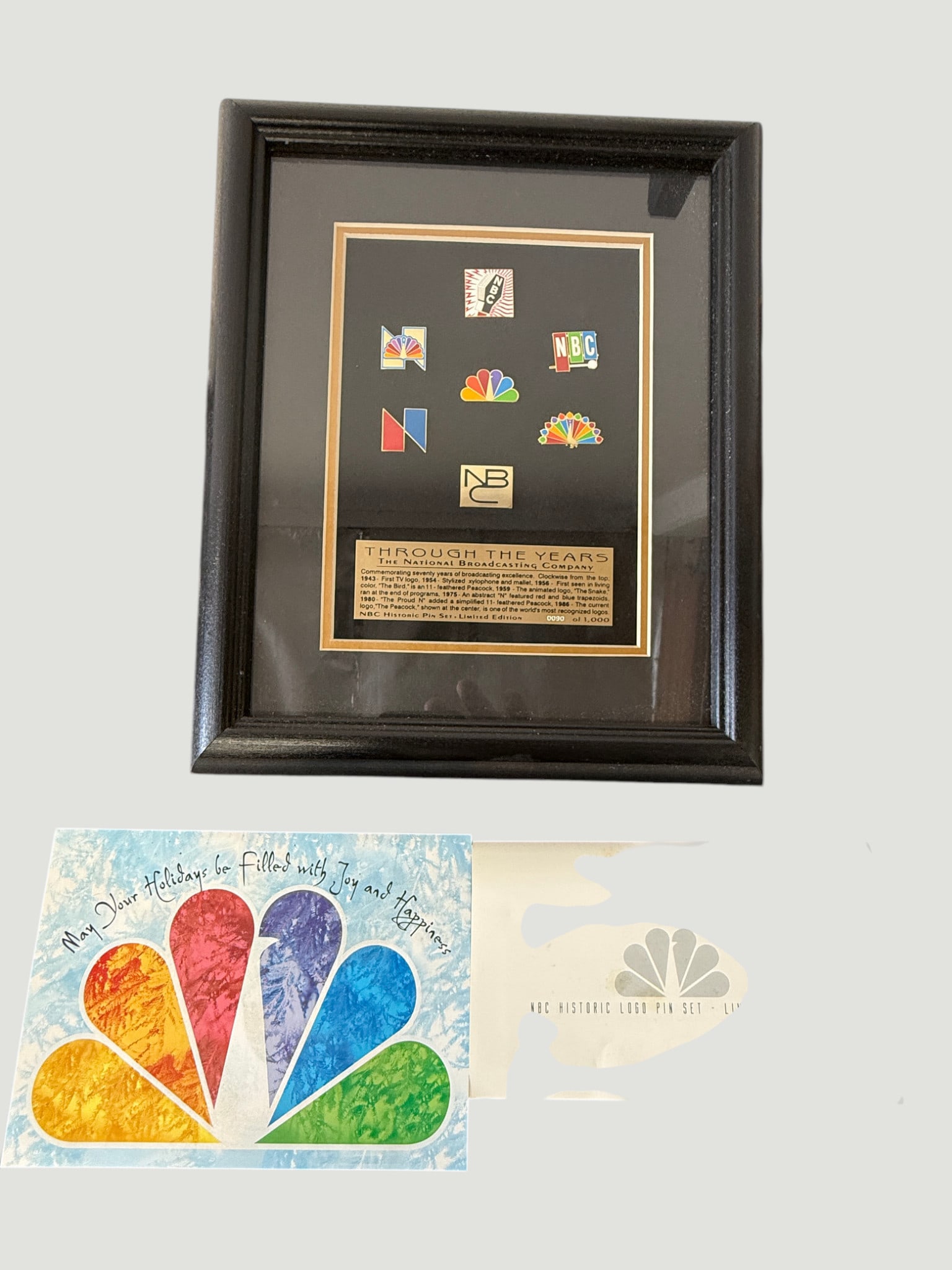 NBC Historic Logo Pin Set Limited Edition Framed — 'Through the Years' c.1990s: A limited edition NBC Historic Logo Pin Set presented in a black shadow box frame with gold matting, featuring seven enamel lapel pins representing the evolution of NBC's broadcast logos from the netw