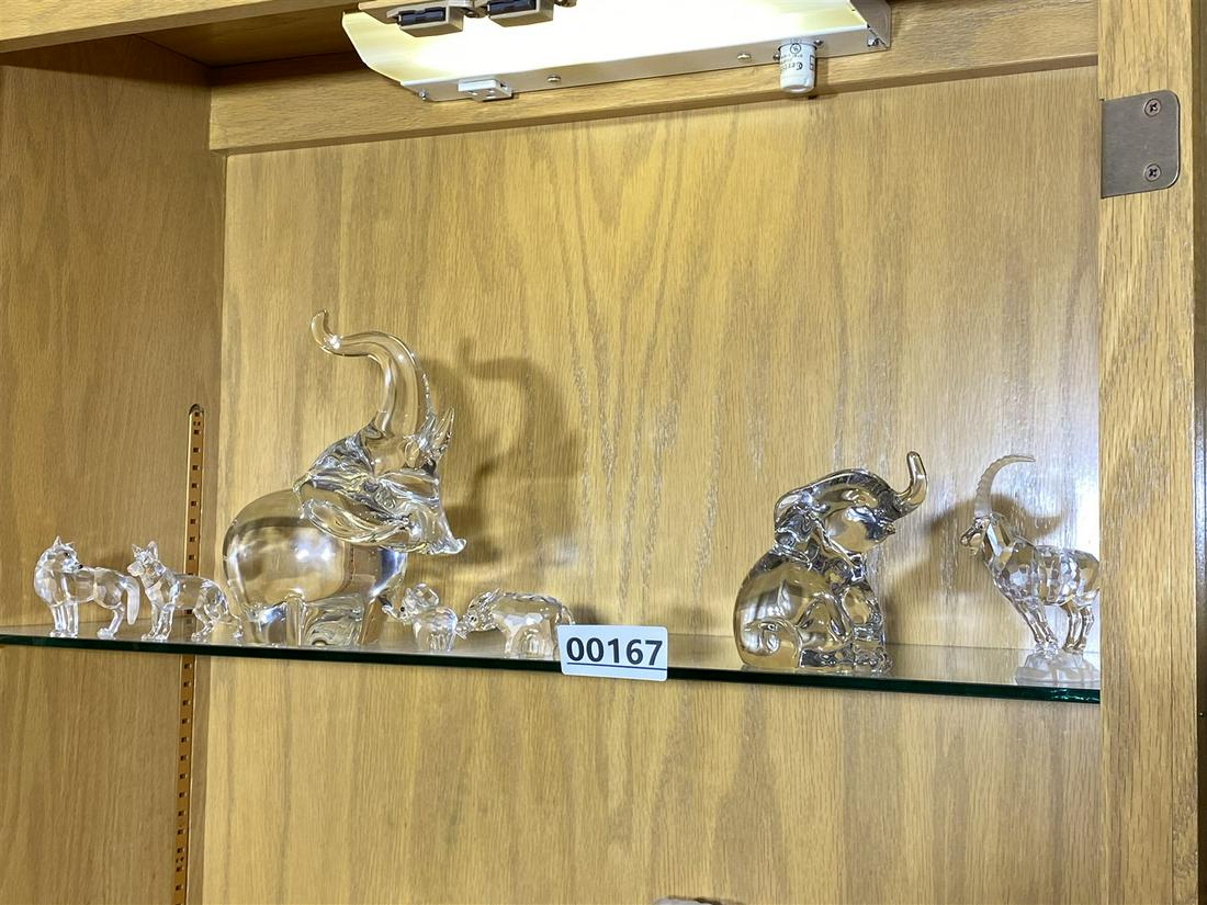 Shelf lot of Steuben, Swarovski, Lenox glass: Large elephant is Steuben and is 7" high. Smaller is Lenox. Other pieces are Swarovski. Free pickup or we'll carefully transport to the shipper for a $8 fee. They will call you to make shipping arrang