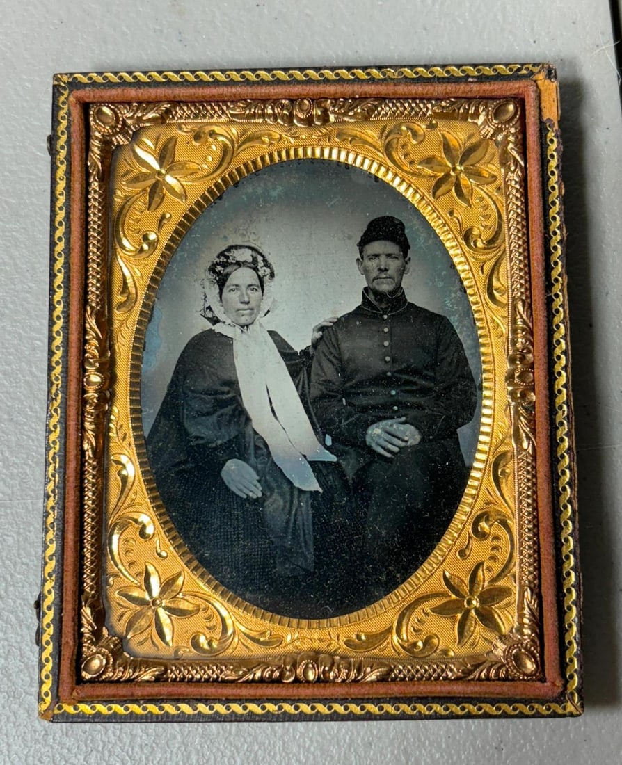 CIVIL WAR TINTYPE OF UNION SOLDIER AND WIFE: Quarter plate tintype seated view of a Civil War Union soldier and his wife. The soldier wears a standard issue enlisted man's nine button frock coat and forage cap. His wife is pictured wearing a spe