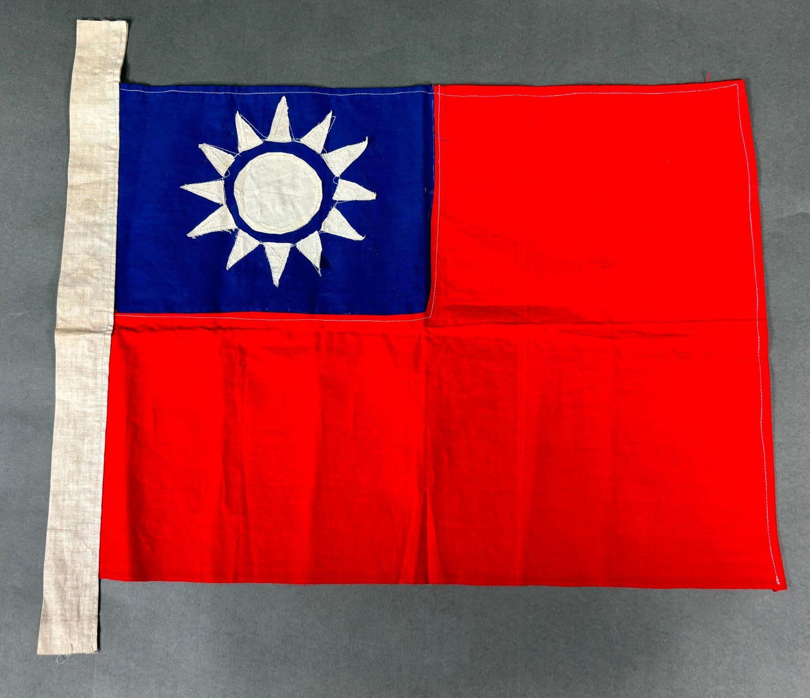 WWII CHINESE FLAG MULTIPIECE CONSTRUCTION: World War Two Chinese flag.This two sided dyed linen flag consists of a seperate blue canton stitched to a red field.The white disc and 12 triangles are separately applied to each side of the canton.