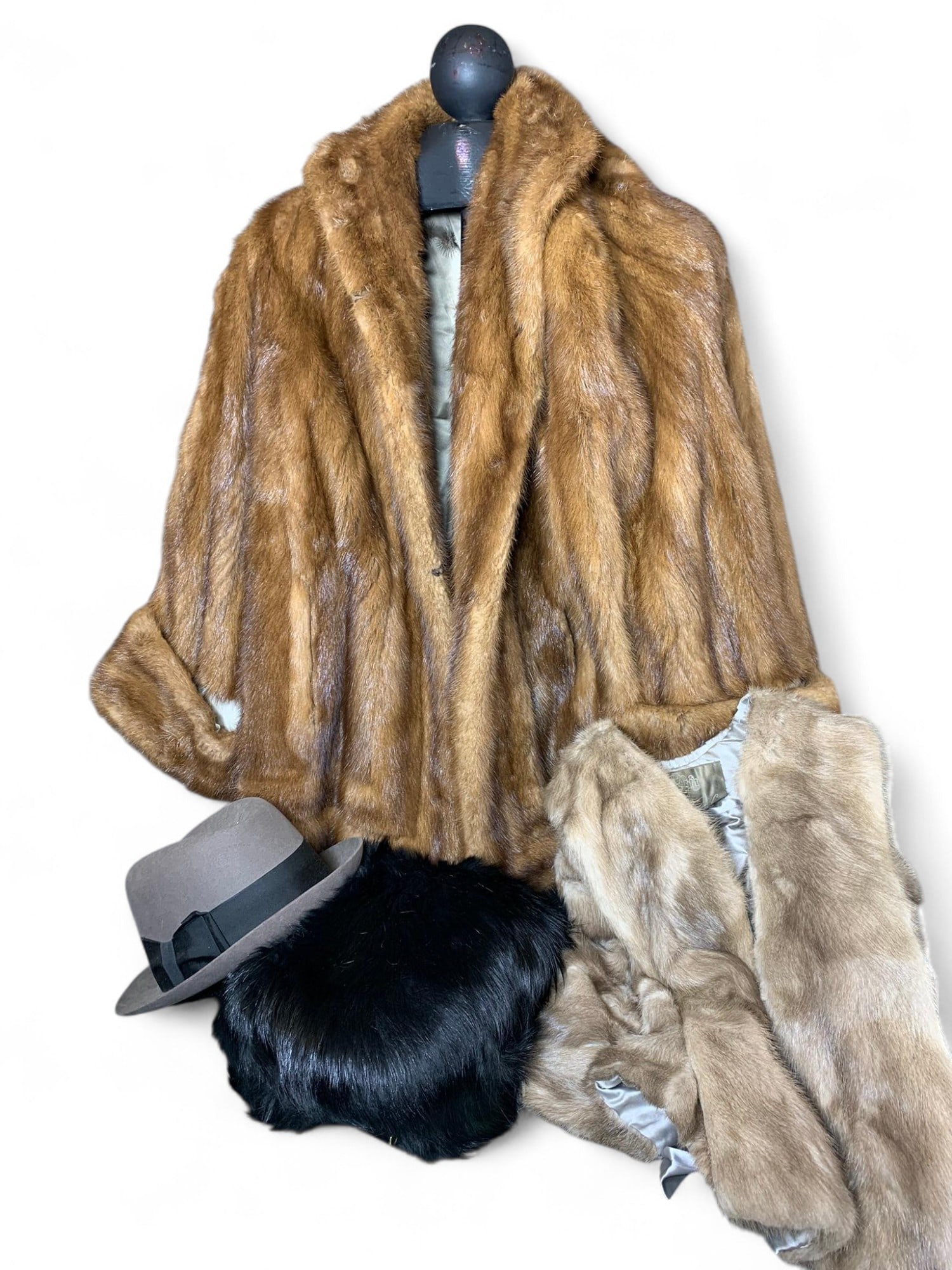 Assorted Fur Apparel Lot - Brown Fur Coat, Tan Fur Vest, Black Fur Hat, Gray Felt Fedora - Brown, Bl: This lot features a collection of elegant fur apparel and a classic felt hat. The items include: 1. A luxurious brown fur coat, likely mink, with a wide collar and spacious cut. 2. A lighter tan or be