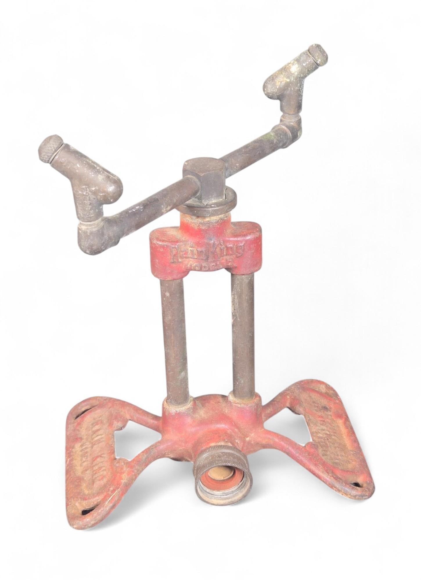 CHICAGO FLEXIBLE SHAFT CO Vintage Red Cast Iron Lawn Sprinkler - Adjustable Nozzles: This item is a vintage lawn sprinkler manufactured by CHICAGO FLEXIBLE SHAFT CO. It features a robust cast iron base, painted in red, supporting a metallic upright structure with a horizontal bar equi