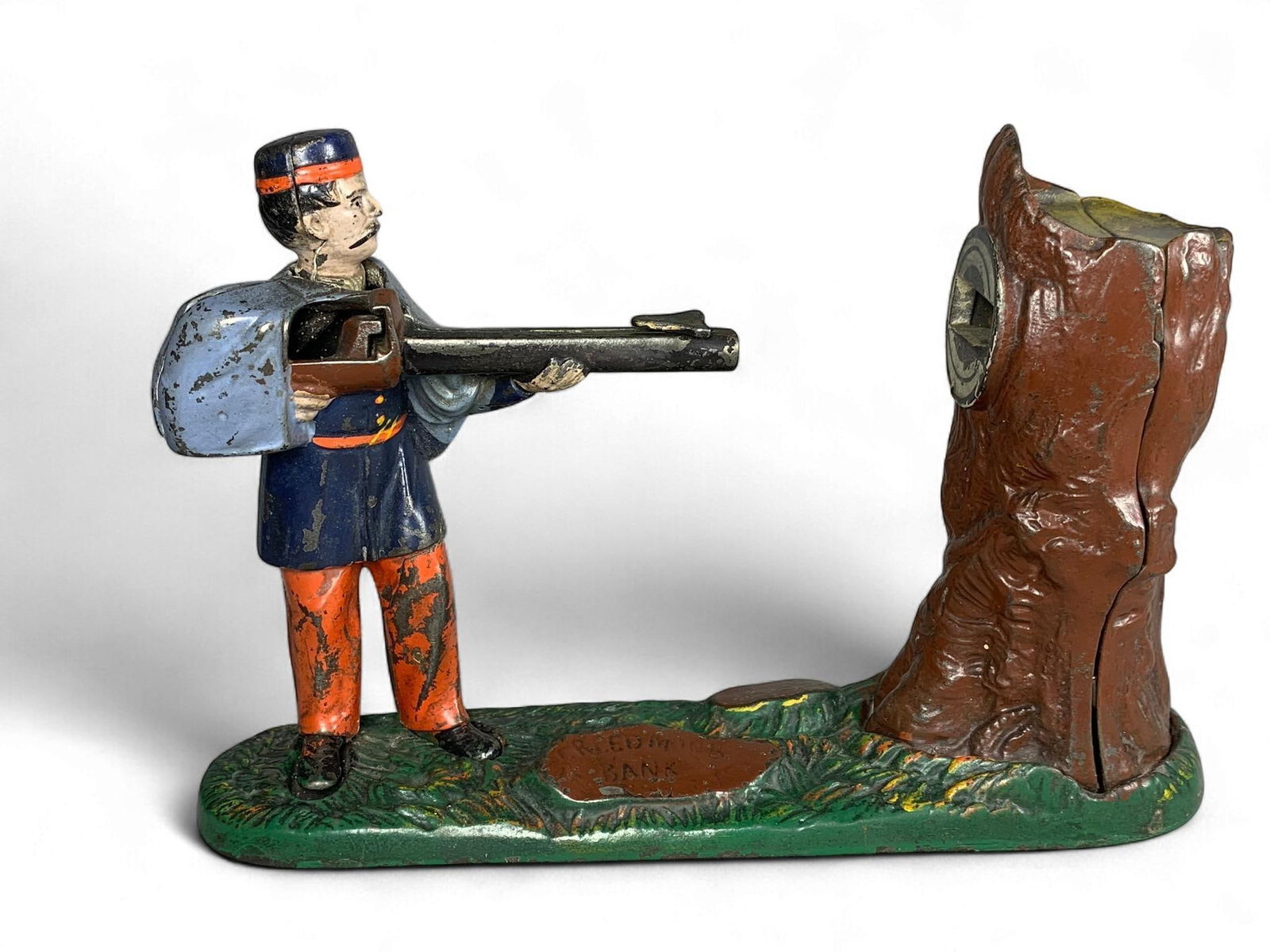 Late 19th Century J&E Stevens Cast Iron Creedmoor Mechanical Bank: A late 19th-century J&E Stevens cast iron Creedmoor mechanical bank, depicting a soldier aiming a rifle at a tree stump. The base is green, sculpted to resemble grass. The coin slot is located in the
