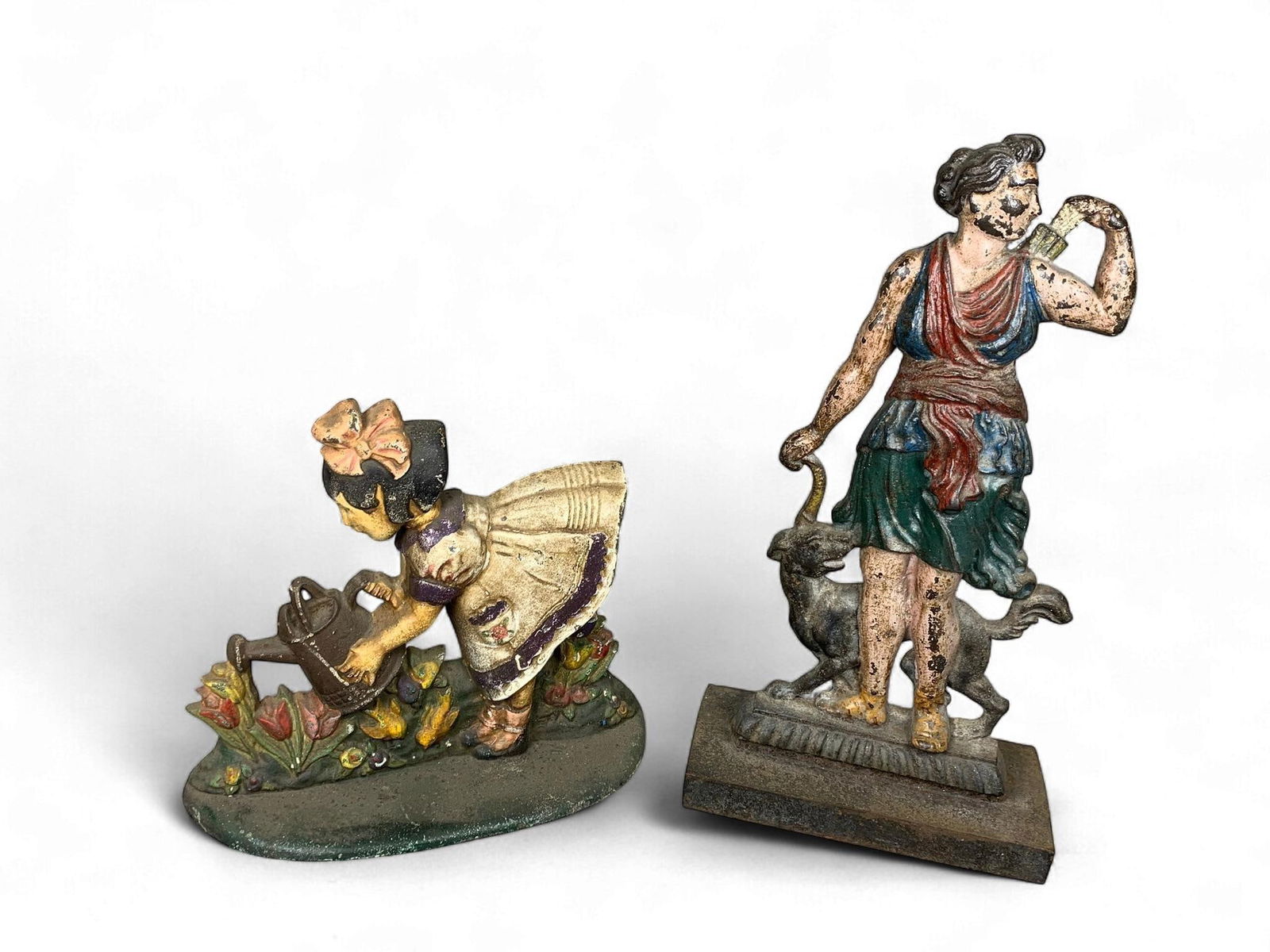 A Group of Antique/Vintage Polychrome Painted Cast Iron Figural Doorstops: A Group of antique or vintage hollow-backed cast iron figural doorstops, originally polychrome painted. The first depicts a young girl in a dress and bow, watering a garden bed with tulips and other f