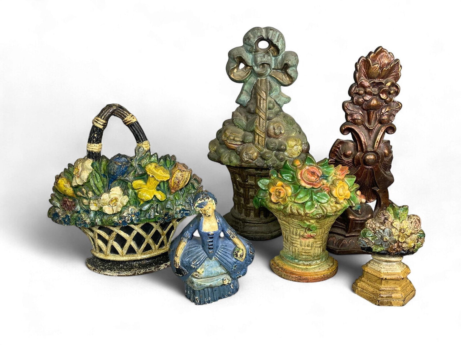 A Group of Polychrome Painted Cast Iron Doorstops: A Group of distinct cast iron decorative objects, predominantly configured as doorstops, featuring various figural and botanical motifs. The grouping includes large baskets overflowing with flowers or