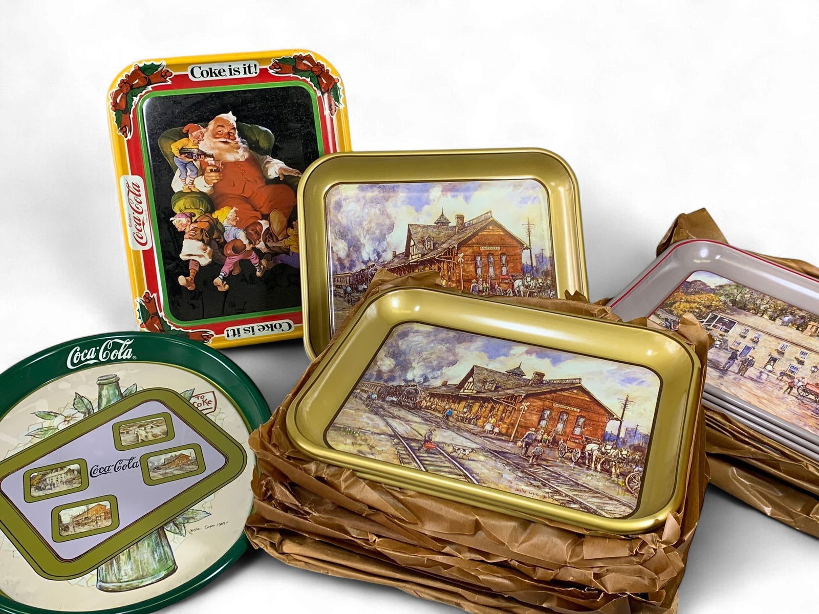 A Collection of Leslie Cope for Zanesville Coca-Cola Commemorative Serving Trays: A collection of Coca-Cola branded collector's serving trays, primarily constructed from enameled tin or metal, featuring various lithographed historical scenes by artist Leslie Cope for The Zanesville