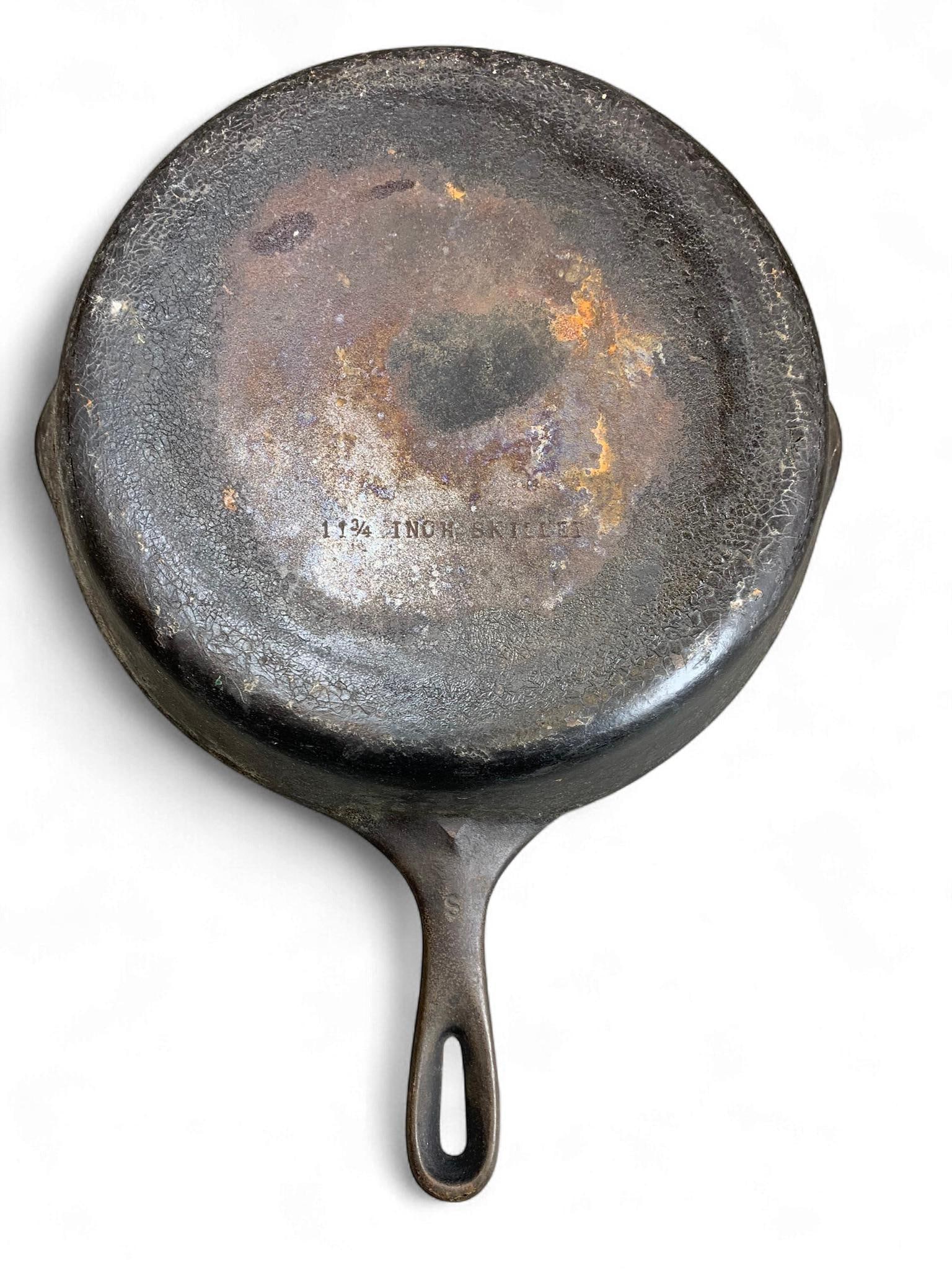 A Vintage Cast Iron Skillet with 'S' Mark, 11 3/4 Inch: A vintage cast iron skillet, constructed from cast iron and marked "11 3/4 INCH SKILLET" on its underside. The handle features a raised 'S' marking near its base. The pan displays a dark, heavily seas