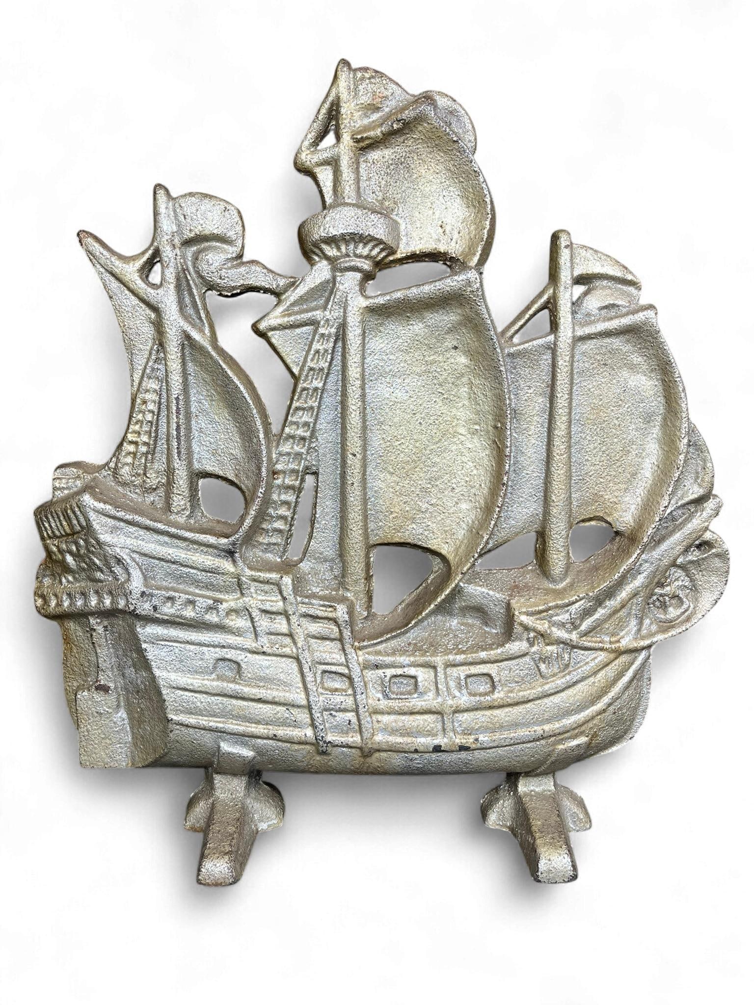 A Cast Iron Sailing Ship Door Stop: A decorative cast iron object, likely functioning as a doorstop or bookend, depicting a multi-masted sailing ship in relief with a flat reverse. The vessel features stylized sails, rigging details, an