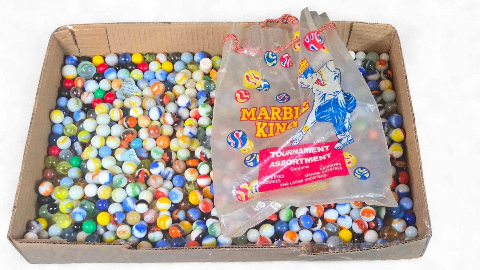A Collection of Vintage Marble King Tournament Assortment Marbles: A collection of vintage glass marbles, primarily identified as a Marble King Tournament Assortment. The lot is housed within a generic cardboard box and includes a clear plastic drawstring bag, brande